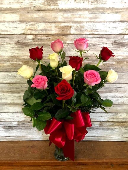 Bouquet of red, pink, and white roses with a red ribbon in a glass vase