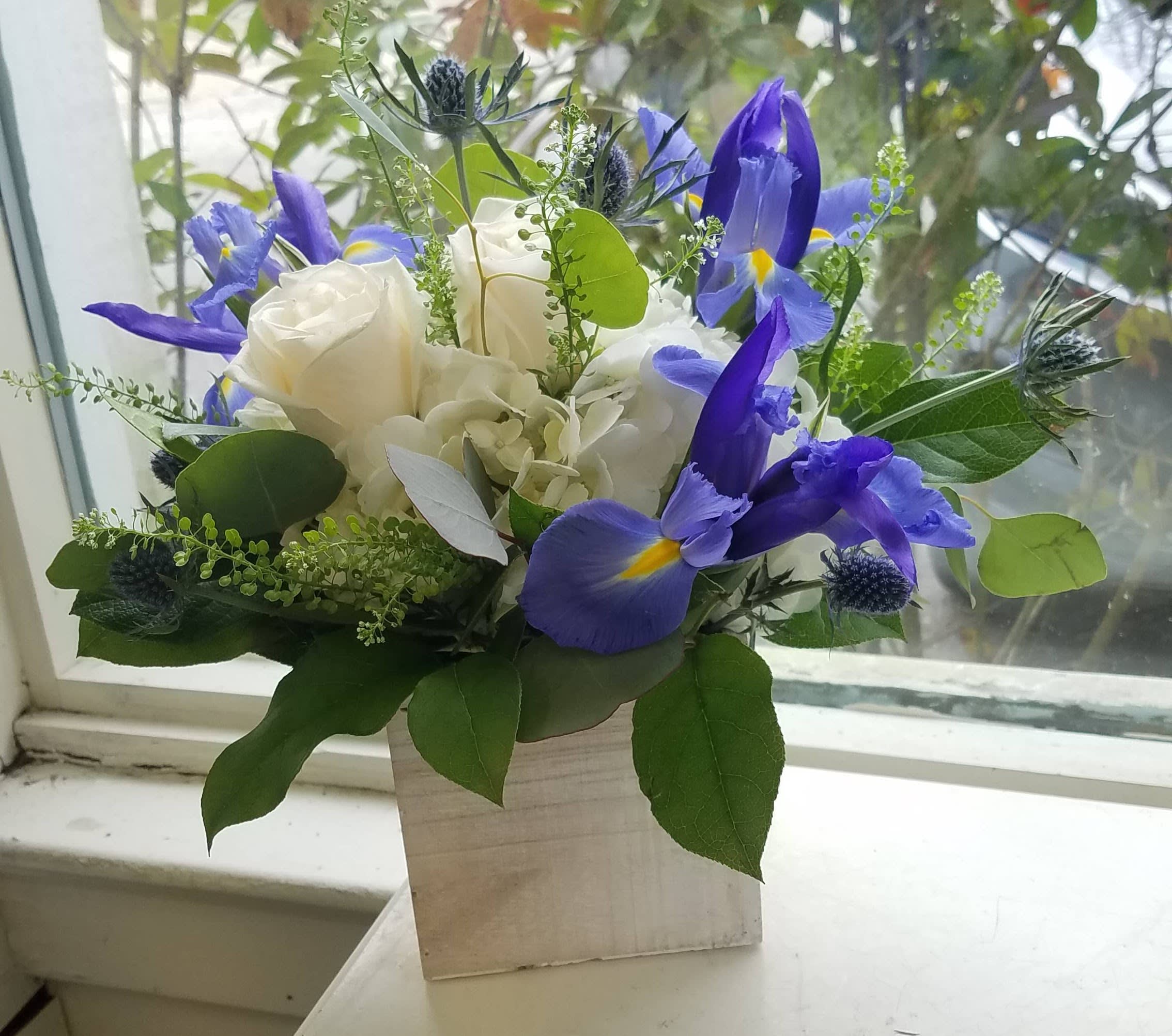 White roses and blue irises arranged in a square wooden vase