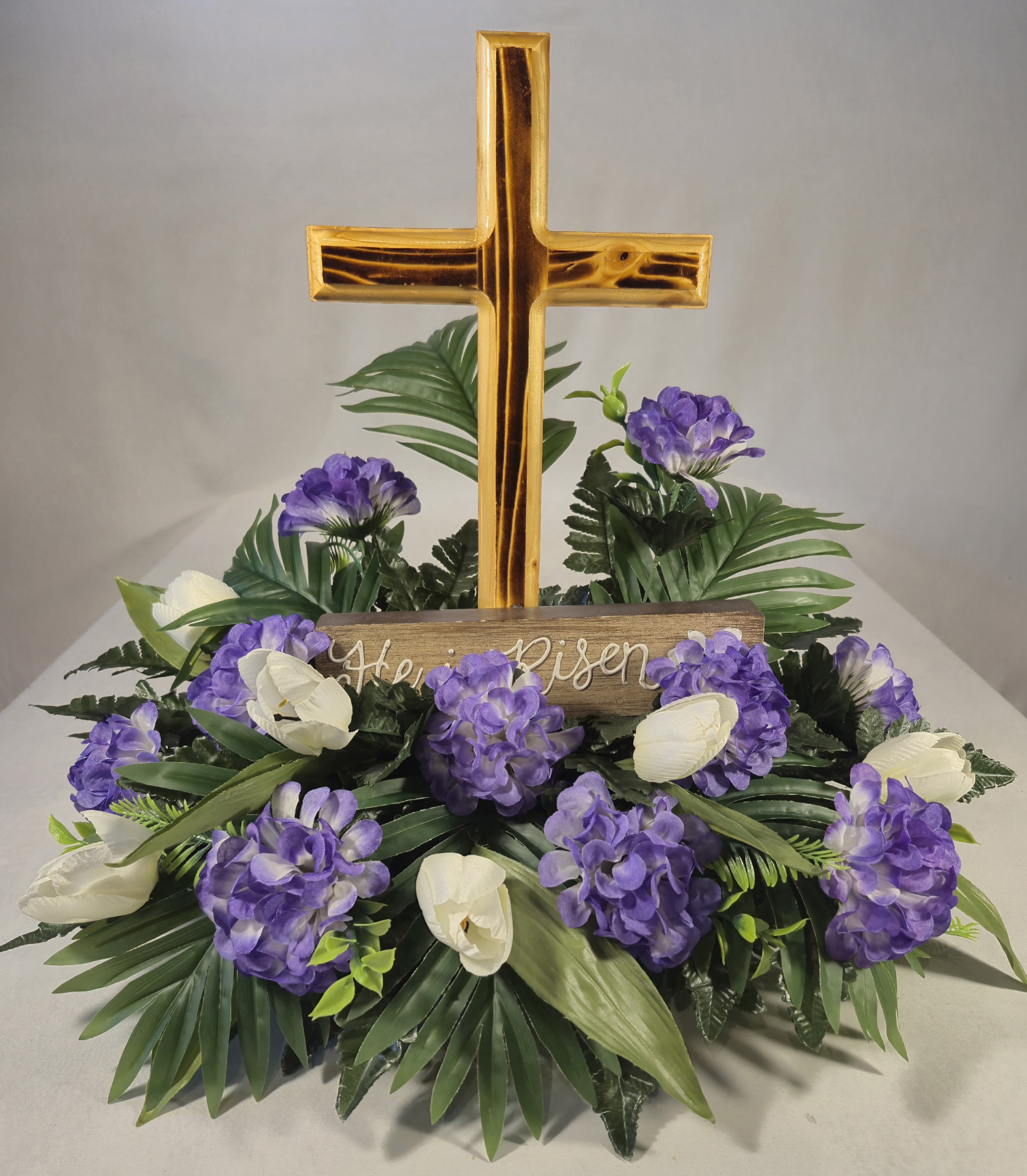 Purple and white floral arrangement with a gold cross centerpiece