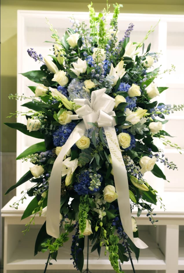 Tall white and blue floral standing spray with a ribbon bow
