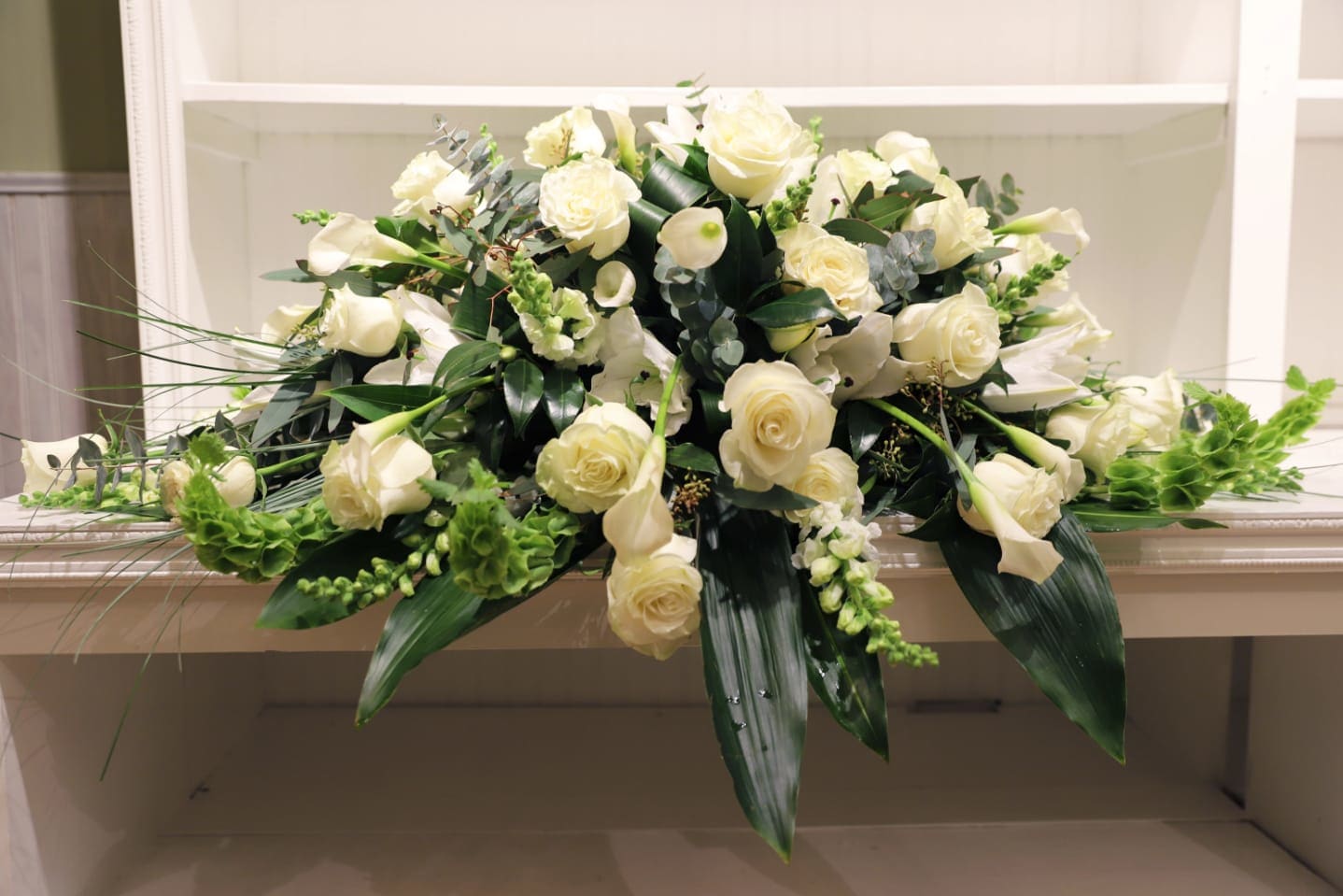 White rose and calla lily arrangement with greenery in a low container