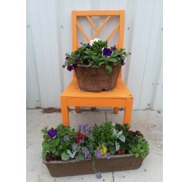 Two brown planters of mixed blooming plants displayed on and in front of an orange chair outdoors