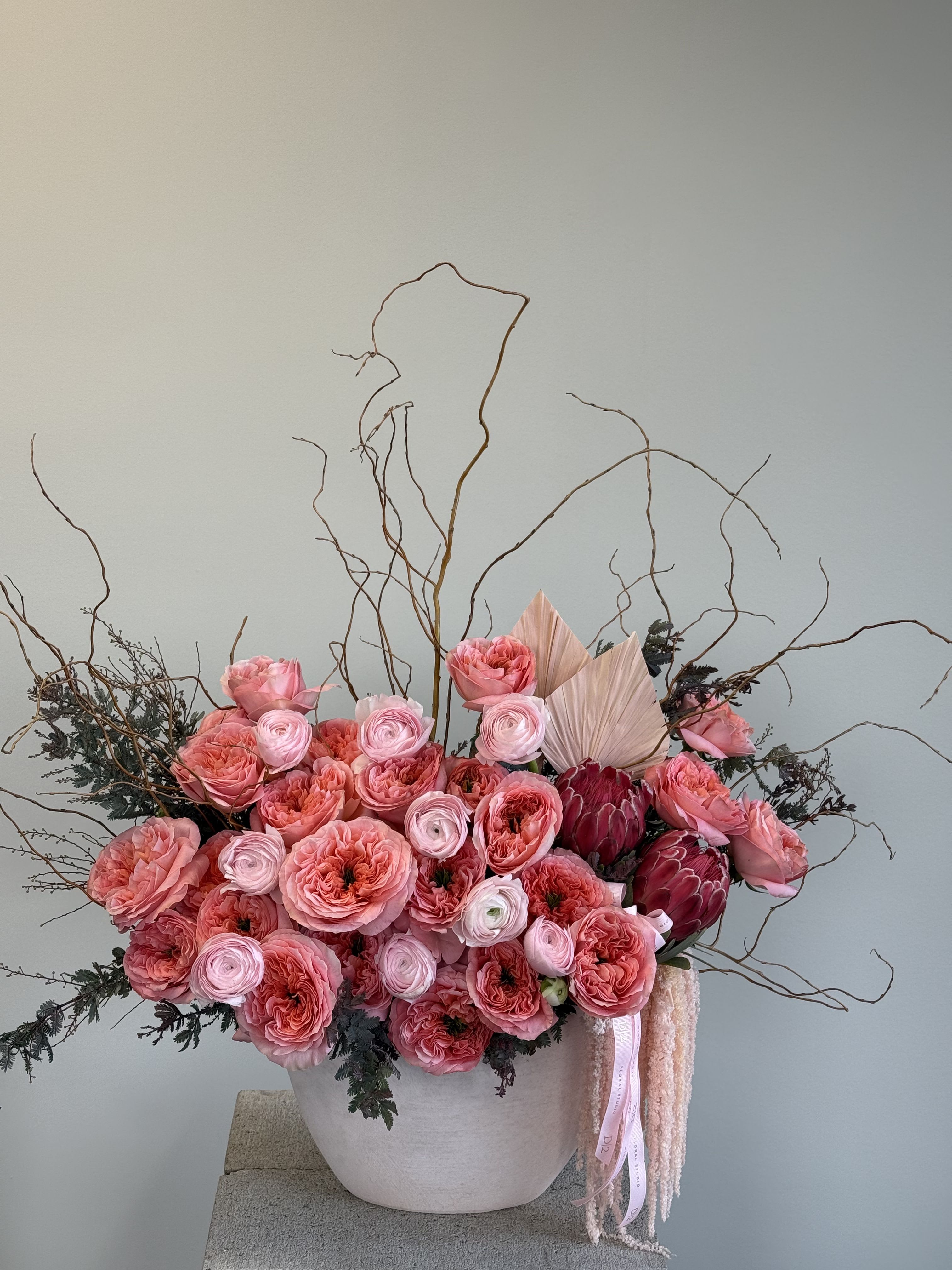 Pink floral arrangement in a white vase with tall curly branches
