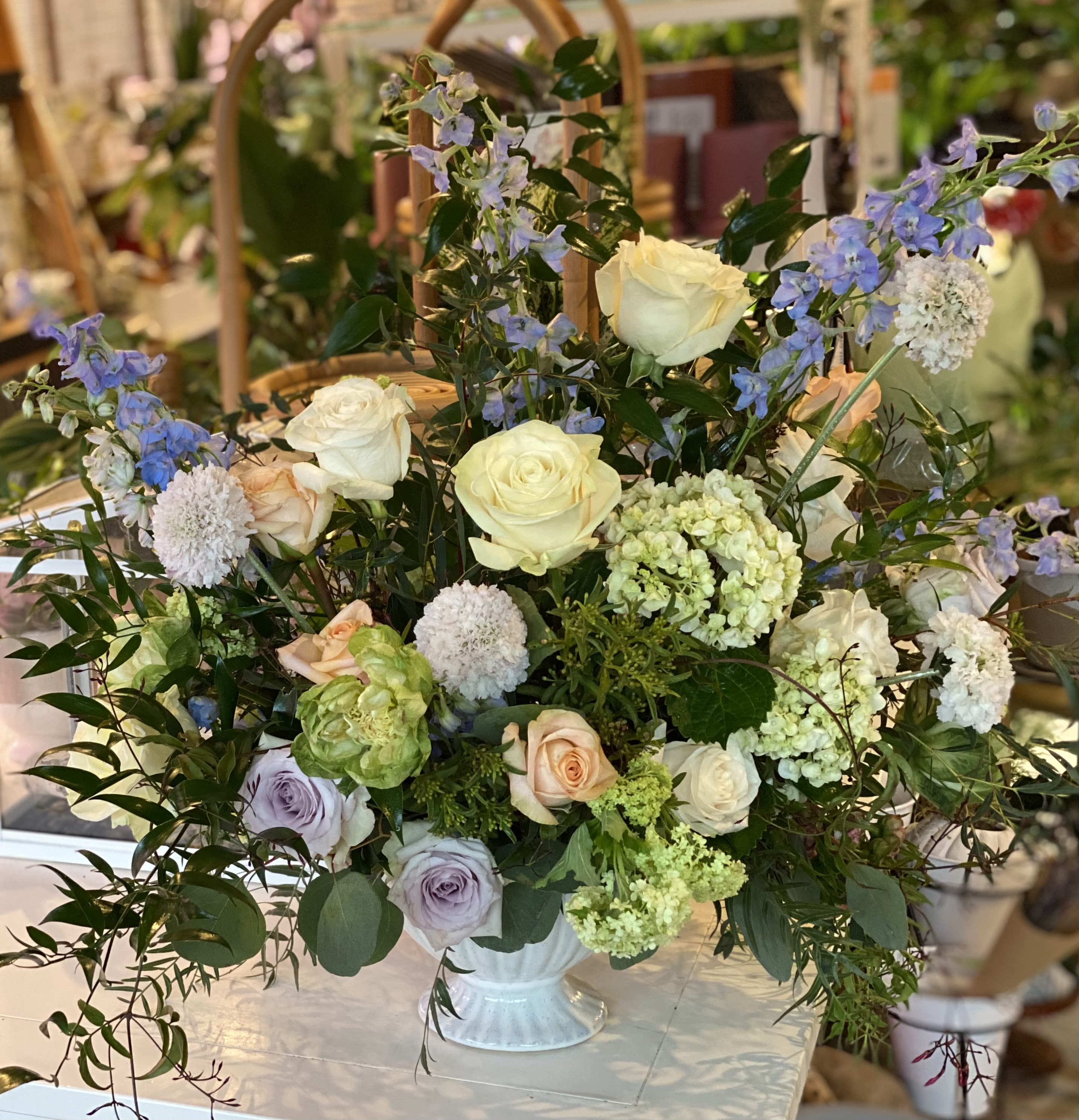 Large mixed floral arrangement in a white vase with roses and blue blossoms