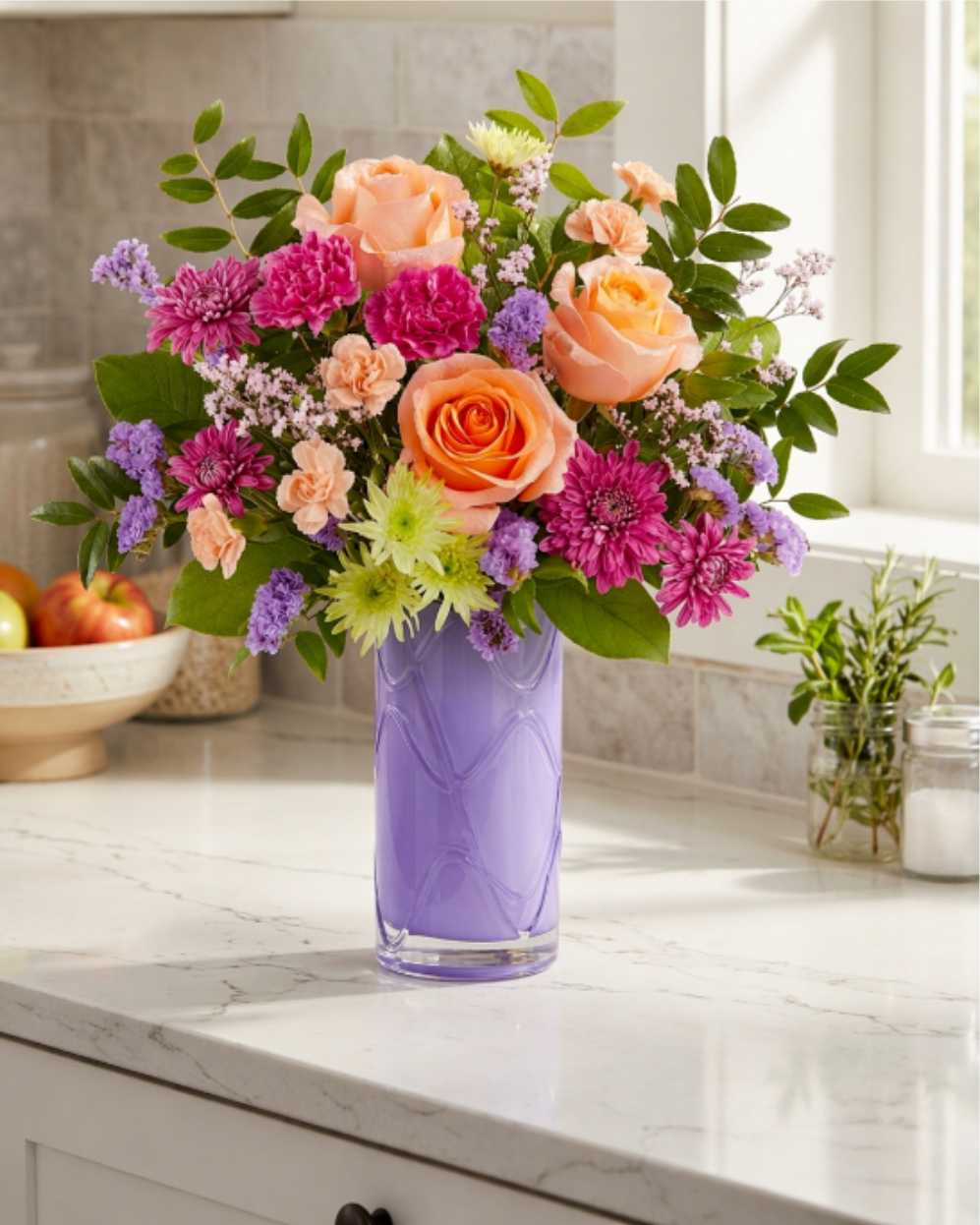 Mixed bouquet of peach roses, pink blooms, and purple flowers in a lavender vase