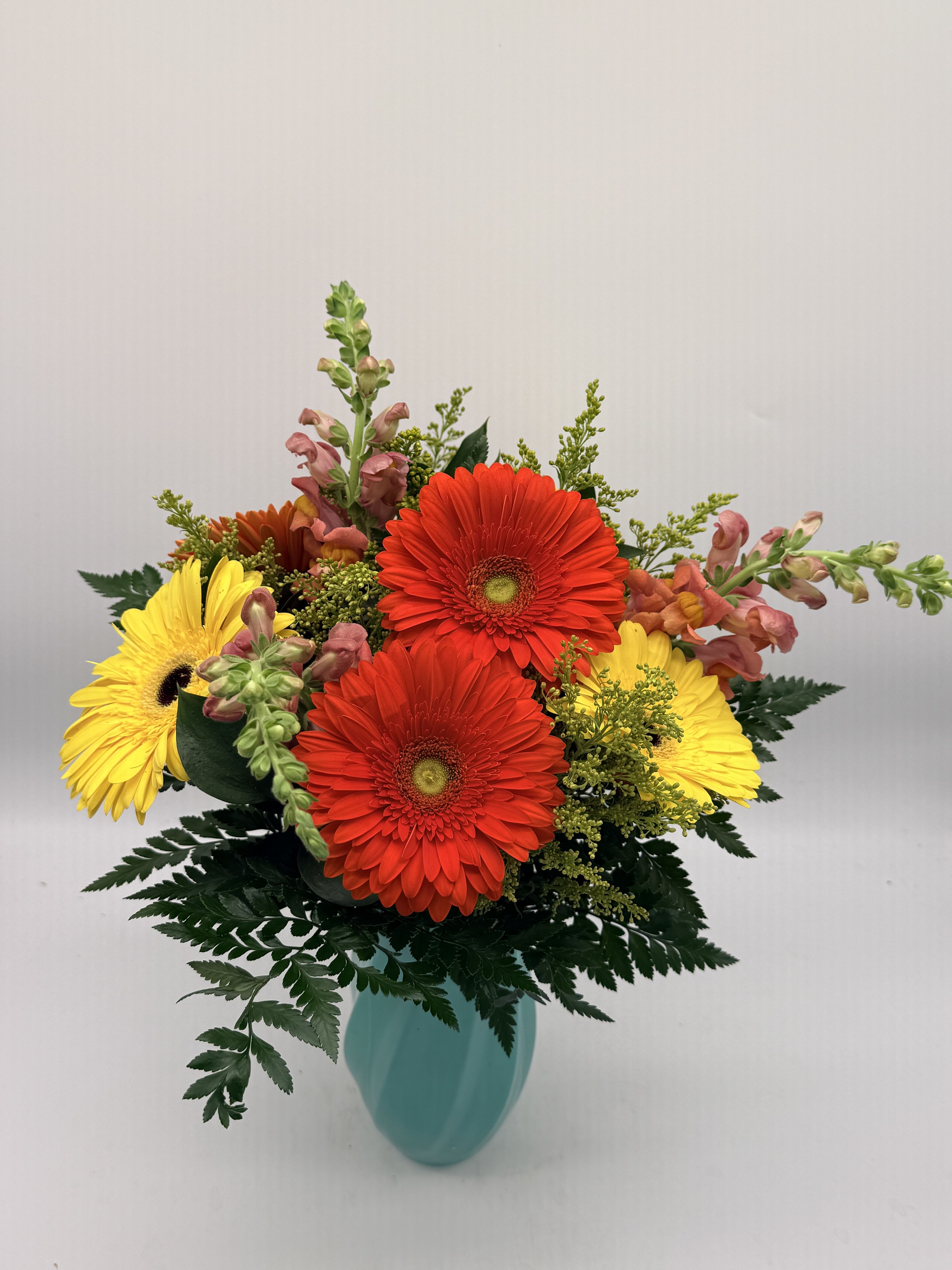 Bright red and yellow gerbera daisies with snapdragons in a teal vase