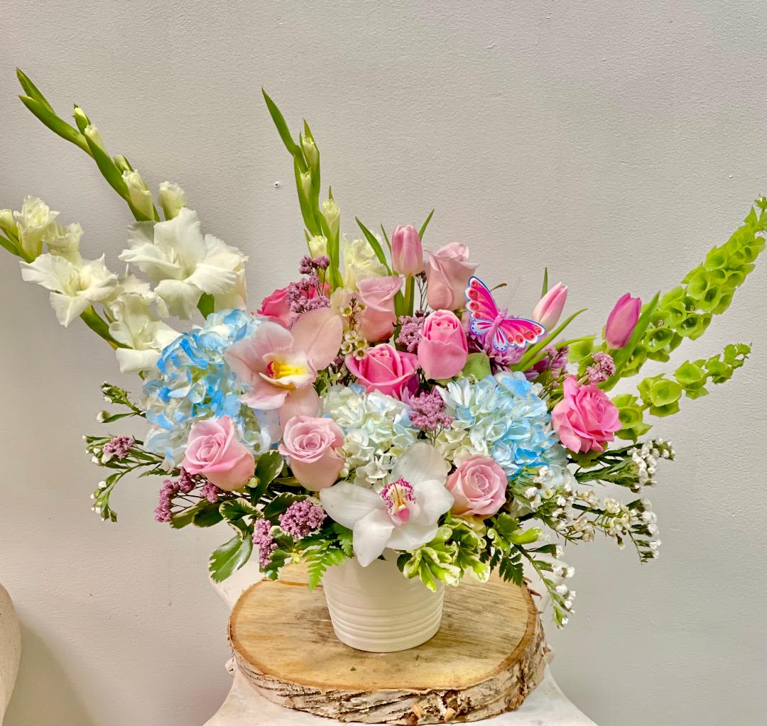 Mixed bouquet of pink roses, orchids, and blue hydrangeas in a white vase