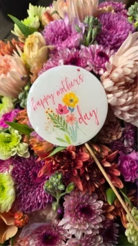 Mother's Love  - Lavender and soft purple chrysanthemums lead a lush, close-packed bouquet that feels like a warm, joyful hug - an ideal Mother's Day arrangement that also translates beautifully for Thinking of You, a new baby visit, holiday cheer, or simply to brighten someone's day. The rounded, hand-tied shape and slightly romantic color story (yellow, pink, peach, lavender, purple, and white) make the recipient feel cherished and celebrated the moment they see it.  Mixed chrysanthemums, tulips, roses and other seasonal blooms are layered for depth and texture, with peach and cream tones softening the vibrant purples and pinks. A round gift tag that reads "happy mothers day" and a discreet wooden stick give the bouquet a polished, gift-ready look while keeping it casual enough for year-round gifting.  Perfect for the person who deserves a thoughtful lift, this compact, dense arrangement fits nicely in a medium vase on arrival. For longest enjoyment, place in fresh water, trim stems at an angle every few days, and keep away from direct heat; the cheerful mix of colors will keep delivering smiles beyond the holiday itself.