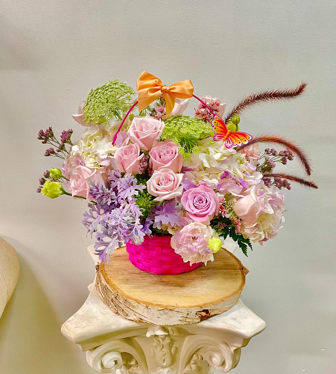 Pink roses and pastel flowers in a bright pink basket with a bow
