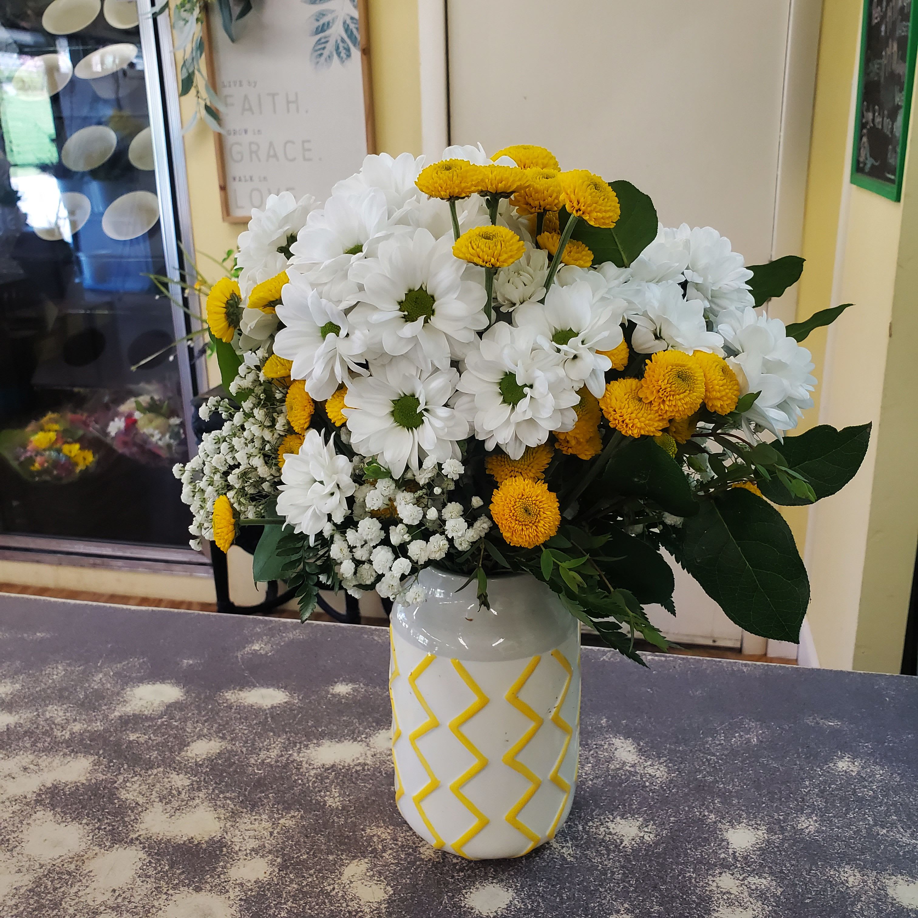 Crazy for Daisies  - A small pedestal vase filled with dark purple daisies, green button poms, assorted natural greens and fill. 