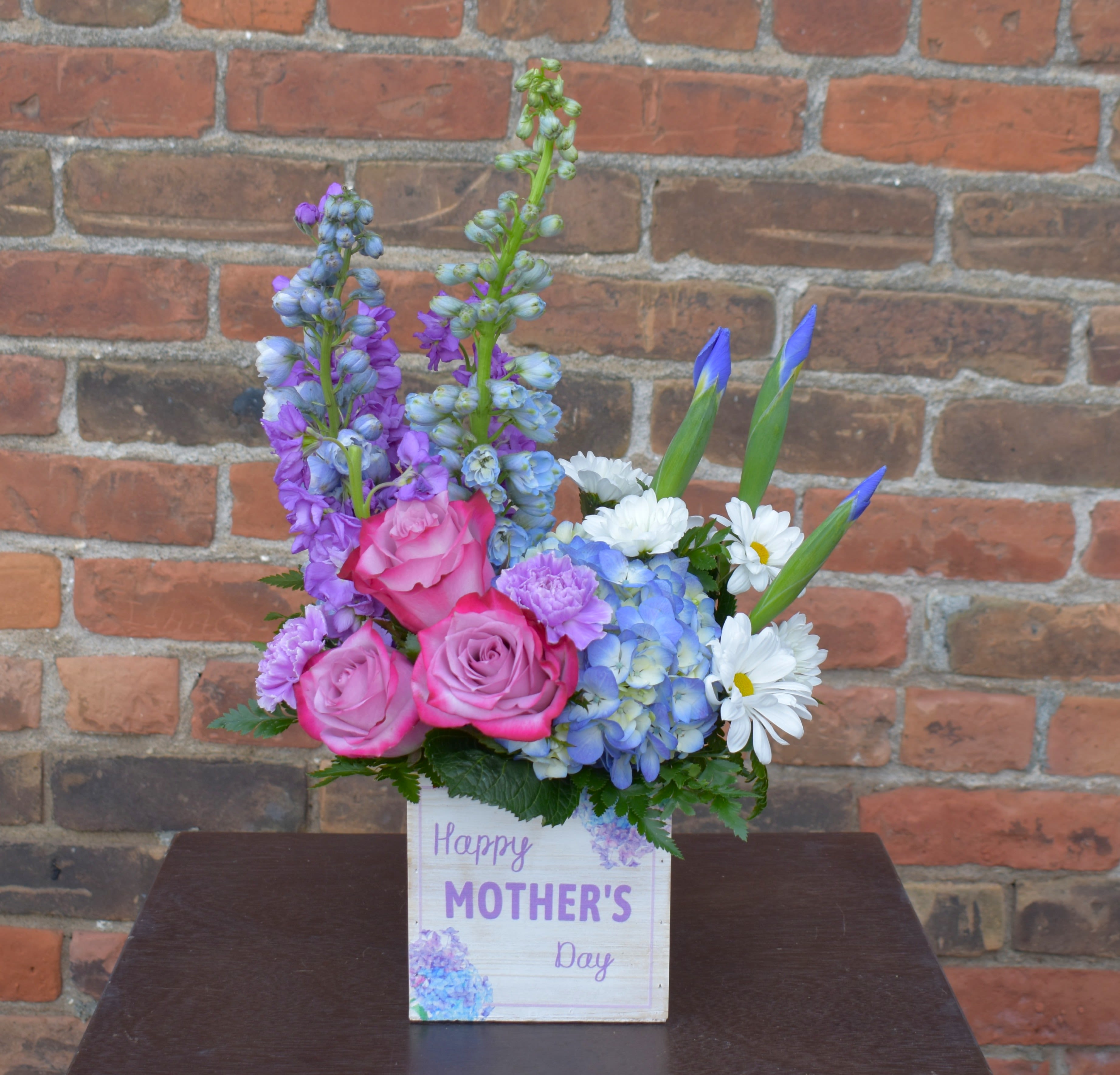Mother's Day Meadow - Every mom deserves a bonus! With beautiful blue delphinium and hydrangea, lavender stock, roses and carnations, white daisies, and accents of greenery all designed in a keepsake wooden Mother's day box, this is the perfect way to celebrate any Mom! 