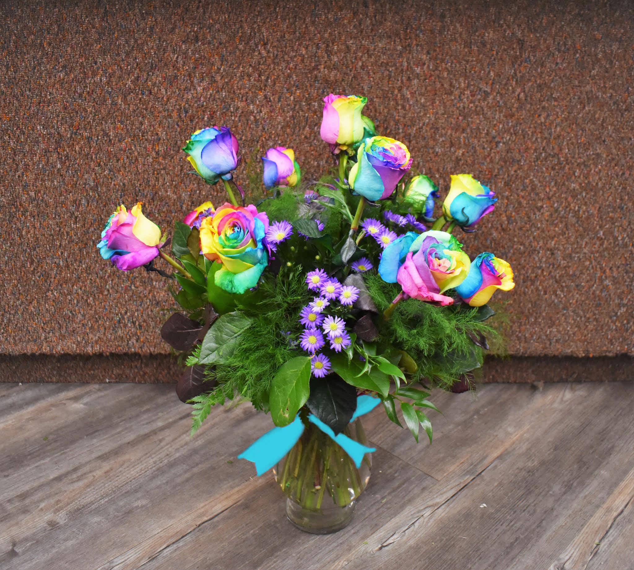 Tie-Dye Dozen - Our Tue-dye rainbow roses are popular for their vibrant and fun color! A dozen roses are designed in a vase and accompanied with greenery, accent flowers, and a bow...the perfect celebration for any occasion! 