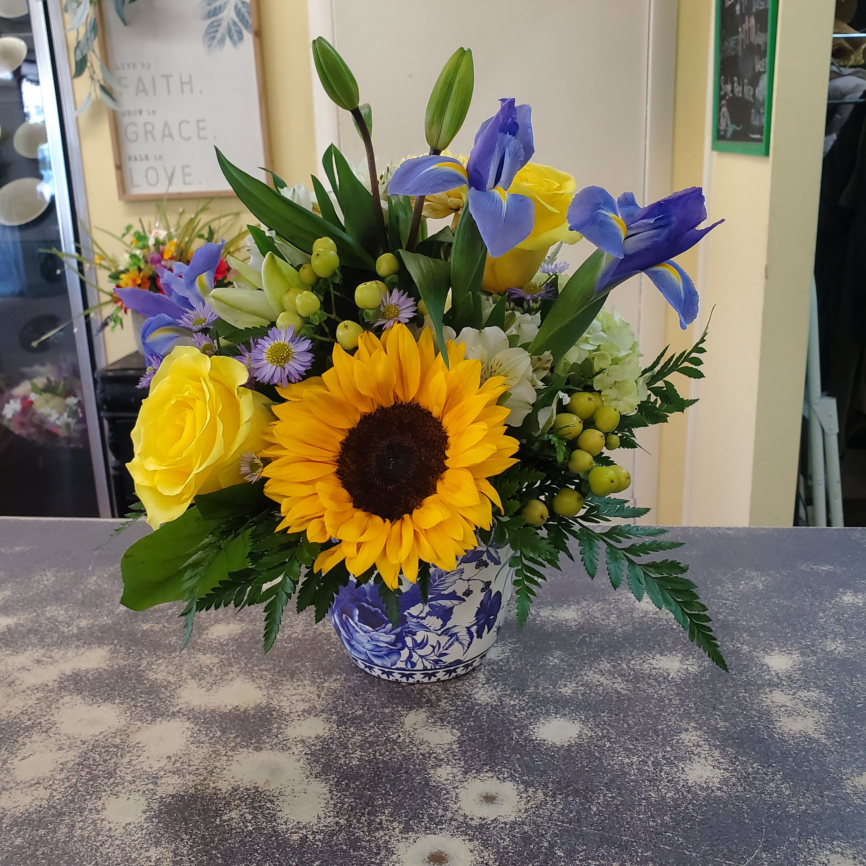French Country  - Blue and white ceramic container filled with assorted seasonal flowers and greens. 