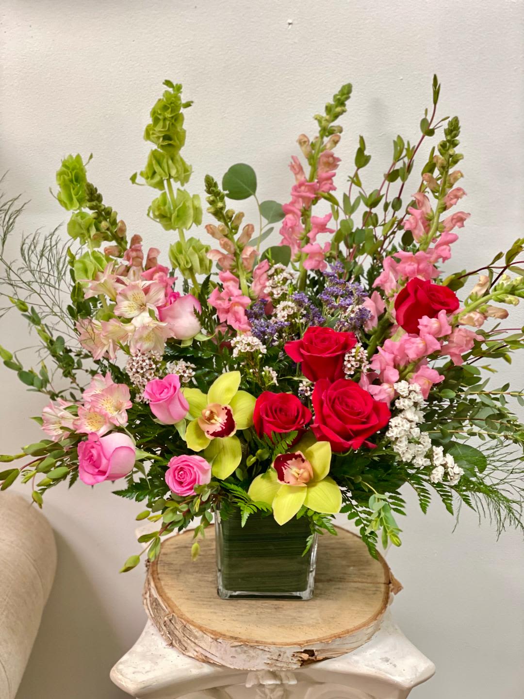Mixed bouquet in a square glass vase with pink, red, and green flowers