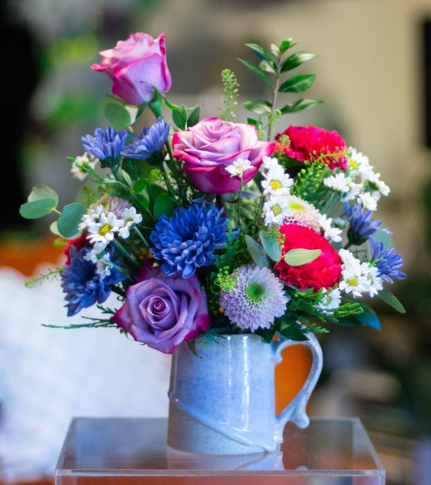 Mixed bouquet of roses and daisies in a blue ceramic mug