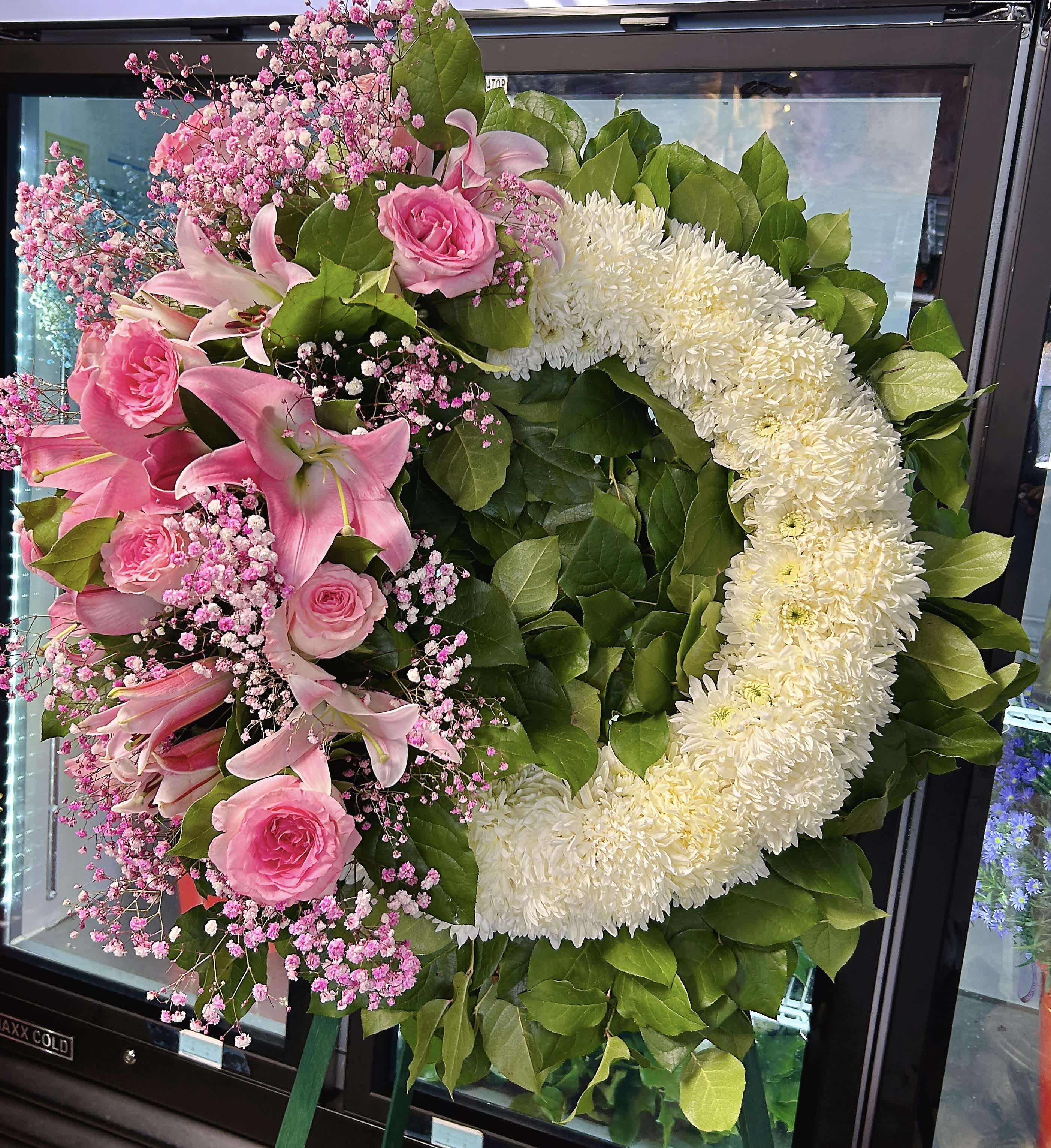 Pink lilies and roses arranged in a heart-shaped wreath with white flowers.
