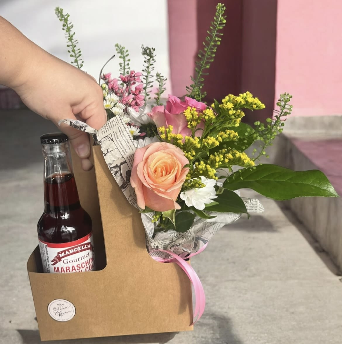 Bouquet with pink and peach roses in a kraft gift box beside a maraschino cherry bottle