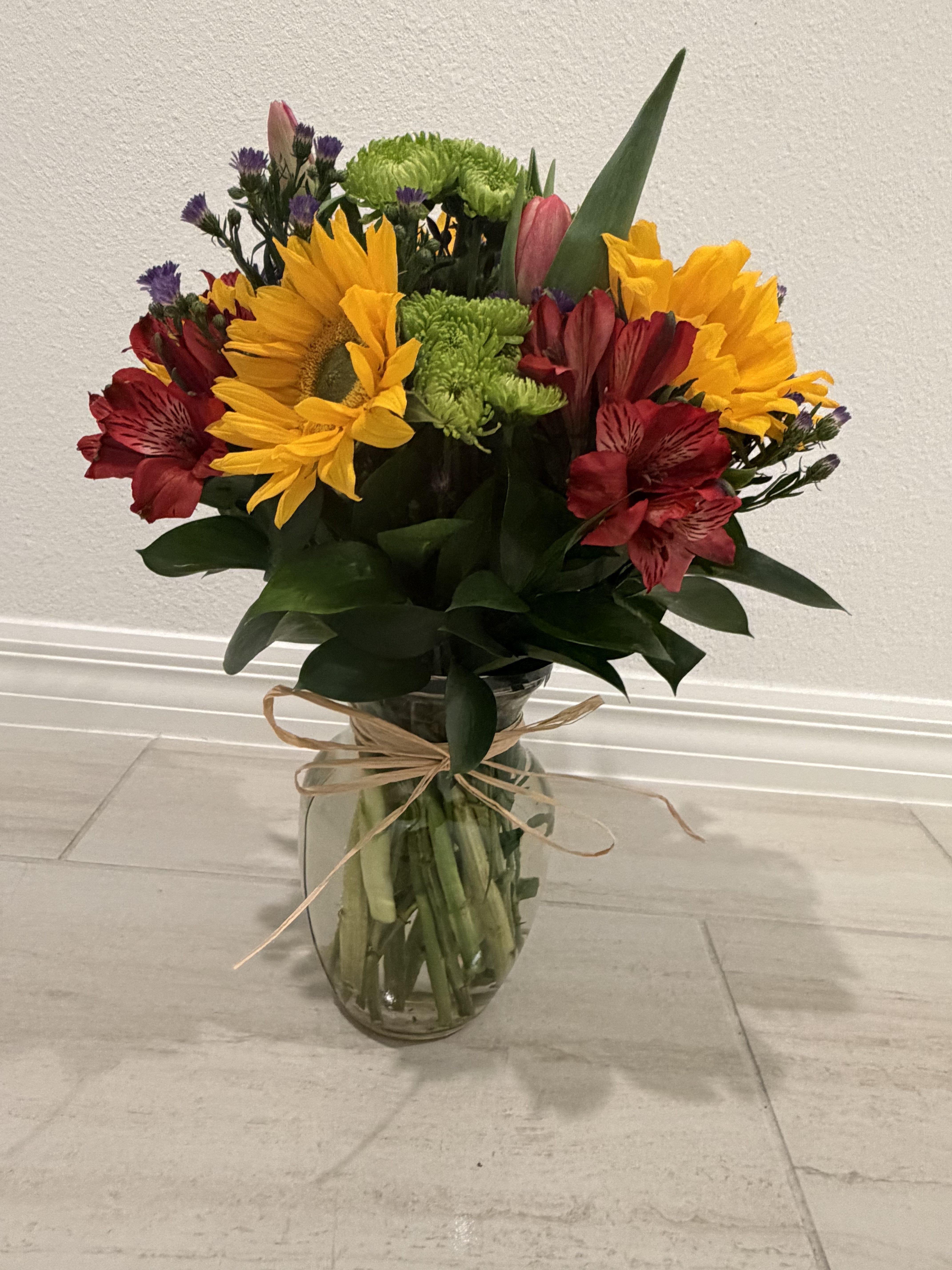 Mixed bouquet of sunflowers, red alstroemeria, and green chrysanthemums in a glass vase