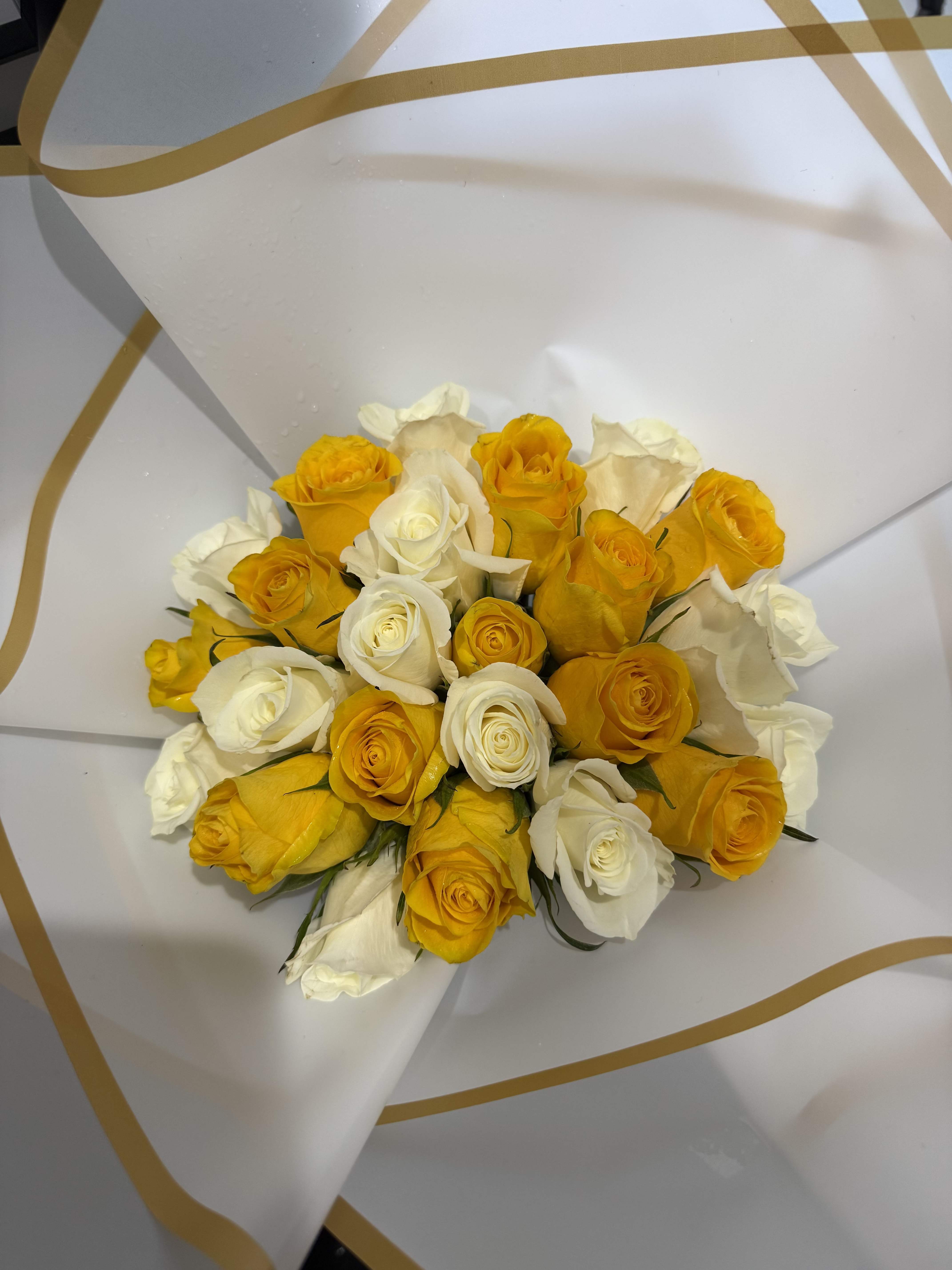 YELLOW AND WHITE  - A bright, tightly clustered hand-tied bouquet of yellow and white roses that instantly reads joyful and elegant - perfect as a birthday bouquet, a thank-you gift, or a fresh spring celebration arrangement. The rounded shape and sunny color contrast make the person you're thinking of feel truly celebrated and noticed the moment they see it.  Classic yellow and white roses are arranged close together for a full, textural look and wrapped in crisp white decorative paper with subtle gold curved accents for a refined finish. The compact hand-tied size makes it easy to carry and display in a simple vase, and the clean presentation keeps the focus on the blooms.  Choose this bouquet for everyday expressions of appreciation, congratulations, or to brighten someone's day; it's the kind of arrangement that reads as both cheerful and sophisticated. For best appearance, trim stems and change water regularly to extend vase life.