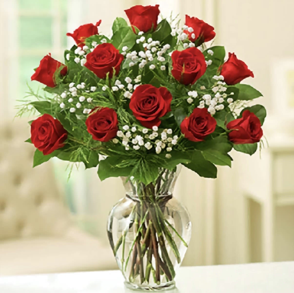 1 DOZEN GLASS  - A classic cluster of red roses with delicate white filler creates an immediate romantic statement-the perfect birthday bouquet, anniversary flowers, or everyday surprise to say "I'm thinking of you." This red-and-white arrangement in a clear glass vase reads timeless and tidy, offering a straightforward, heartfelt gift that makes the recipient feel cherished and noticed.  A dozen red roses are arranged in a rounded, balanced bouquet with small white blooms woven through for contrast and texture. Stems are visible through the water in the clear glass vase for a clean, traditional presentation; overall size and proportions suit a tabletop or mantel. Ideal for anniversaries, birthdays, or a sincere thank-you, this arrangement arrives ready to display-simply change the water and trim stems every few days to keep blooms fresh.