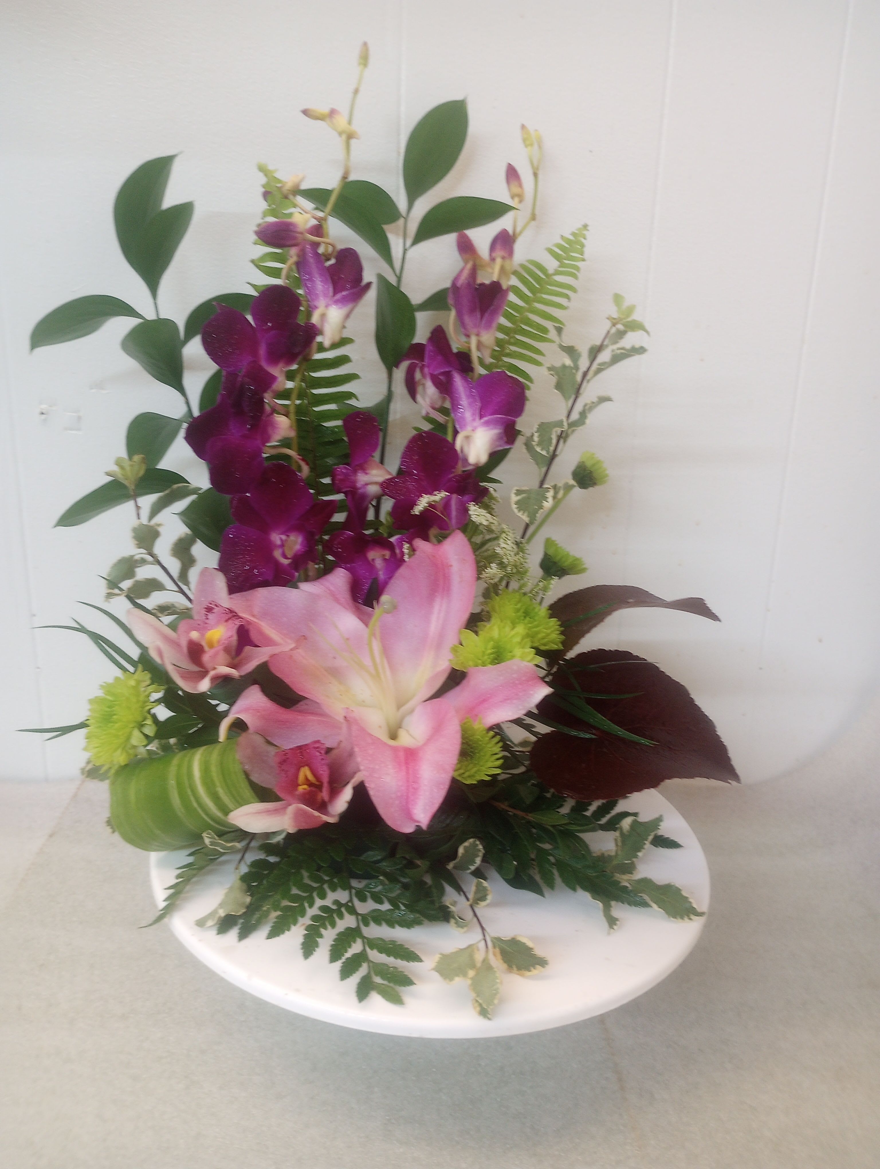 Take me away - A single large pink lily and upright purple orchid sprays give this flower arrangement a bright, tropical lift. 