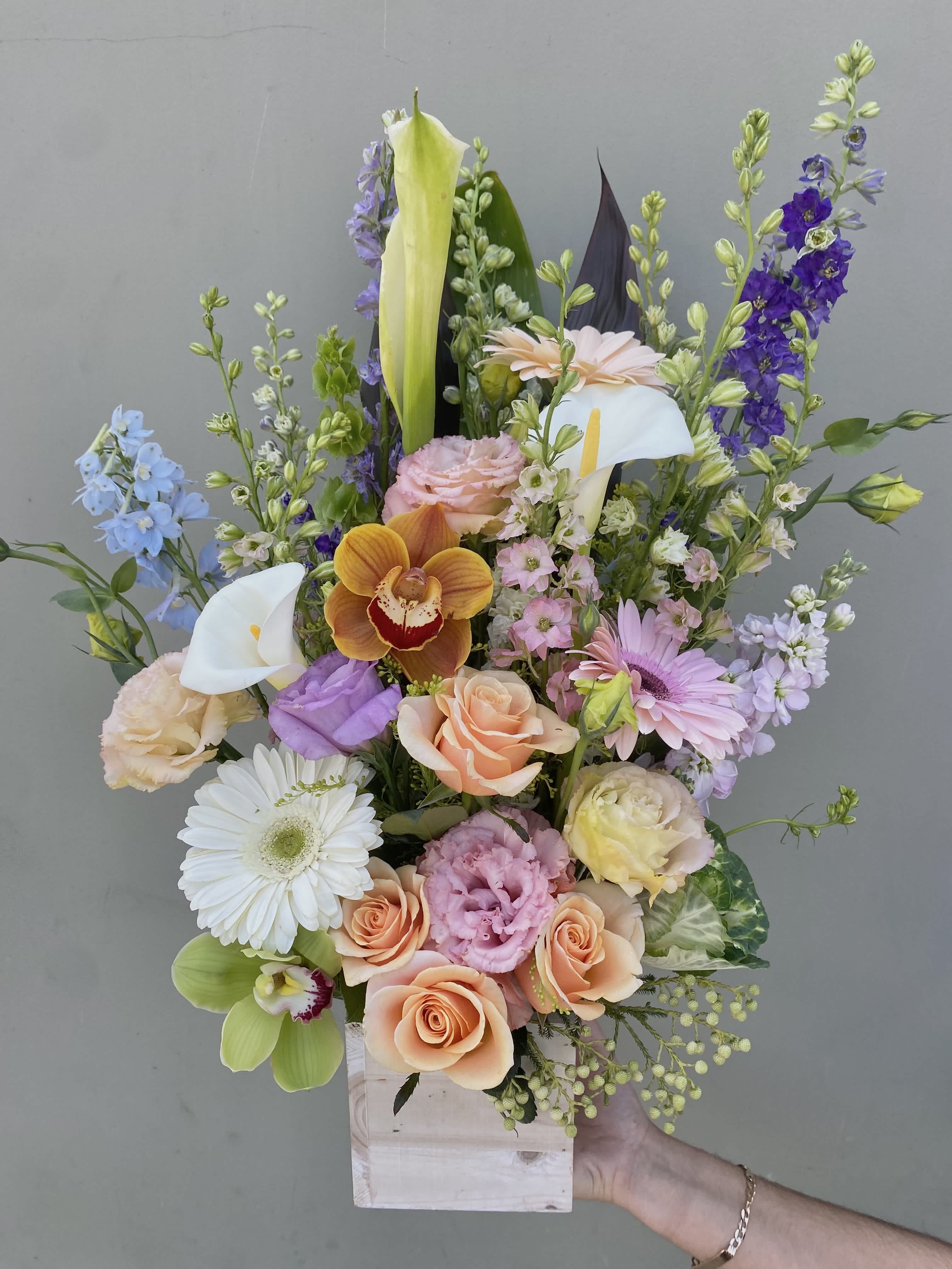 Mixed pastel flower arrangement in a wooden box with orchids and roses
