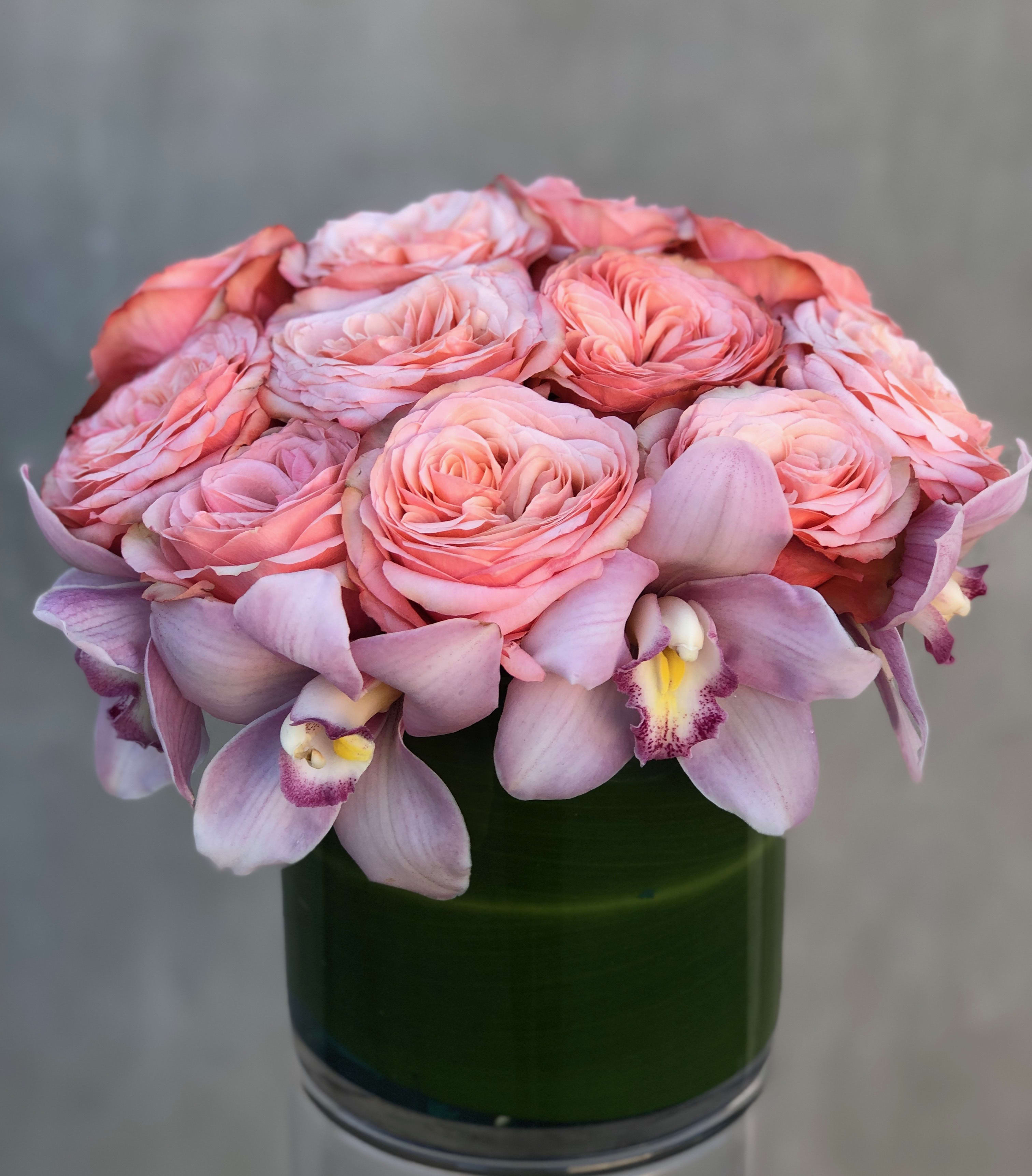 Pink roses and lavender orchids arranged in a green glass vase