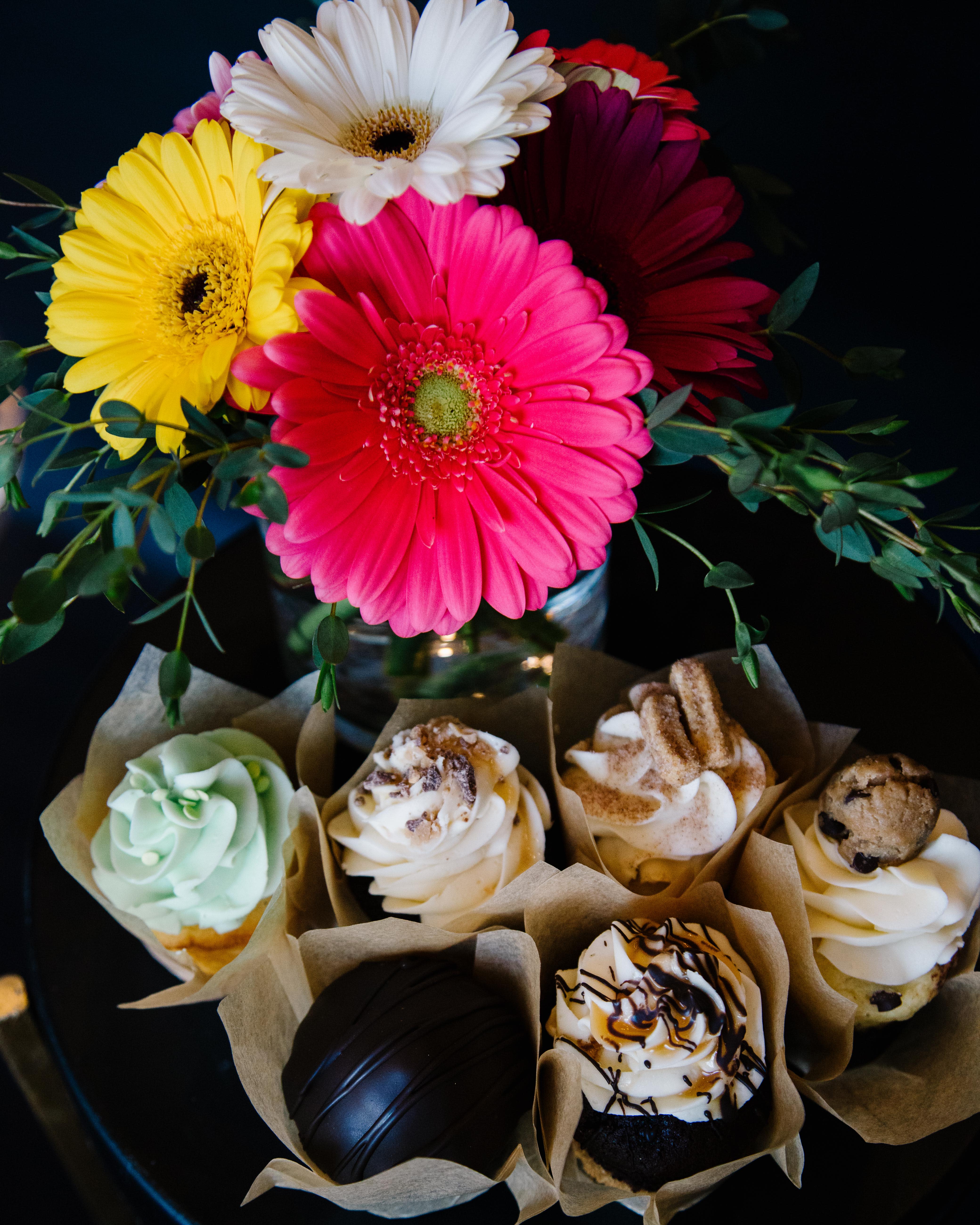 Bright gerbera daisies in a vase above assorted cupcakes