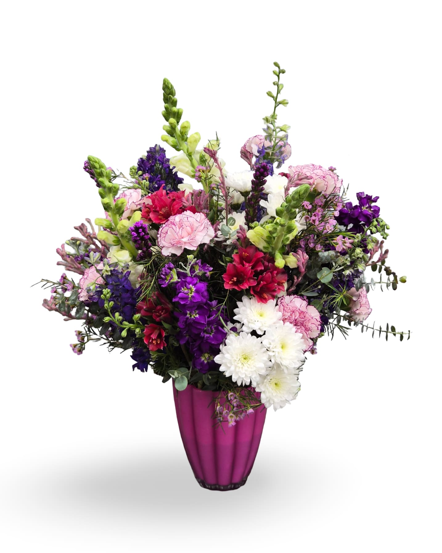 Blooming Meadow - A lively, colorful arrangement that reads like a blooming meadow - perfect as an anniversary, birthday, Mother's Day, or just-because gift. This upright bouquet in a tall pink vase mixes pinks, purples, whites, and fresh greens so the person you're thinking of will feel celebrated and uplifted; its spiky snapdragons give height while rounded carnations and daisy-like blooms fill the base for a joyful, spring-ready look.  This design features larkspur, carnations, white mums, liatris, snapdragons dragons and stock,  arranged densely for a full, textured silhouette. Comes in a pink glass vase; arrangement measures approximately 21" x 22". Ideal for thank-you gestures, get-well wishes, or to mark a special milestone, and easy to refresh with regular water changes to keep blooms vibrant.
