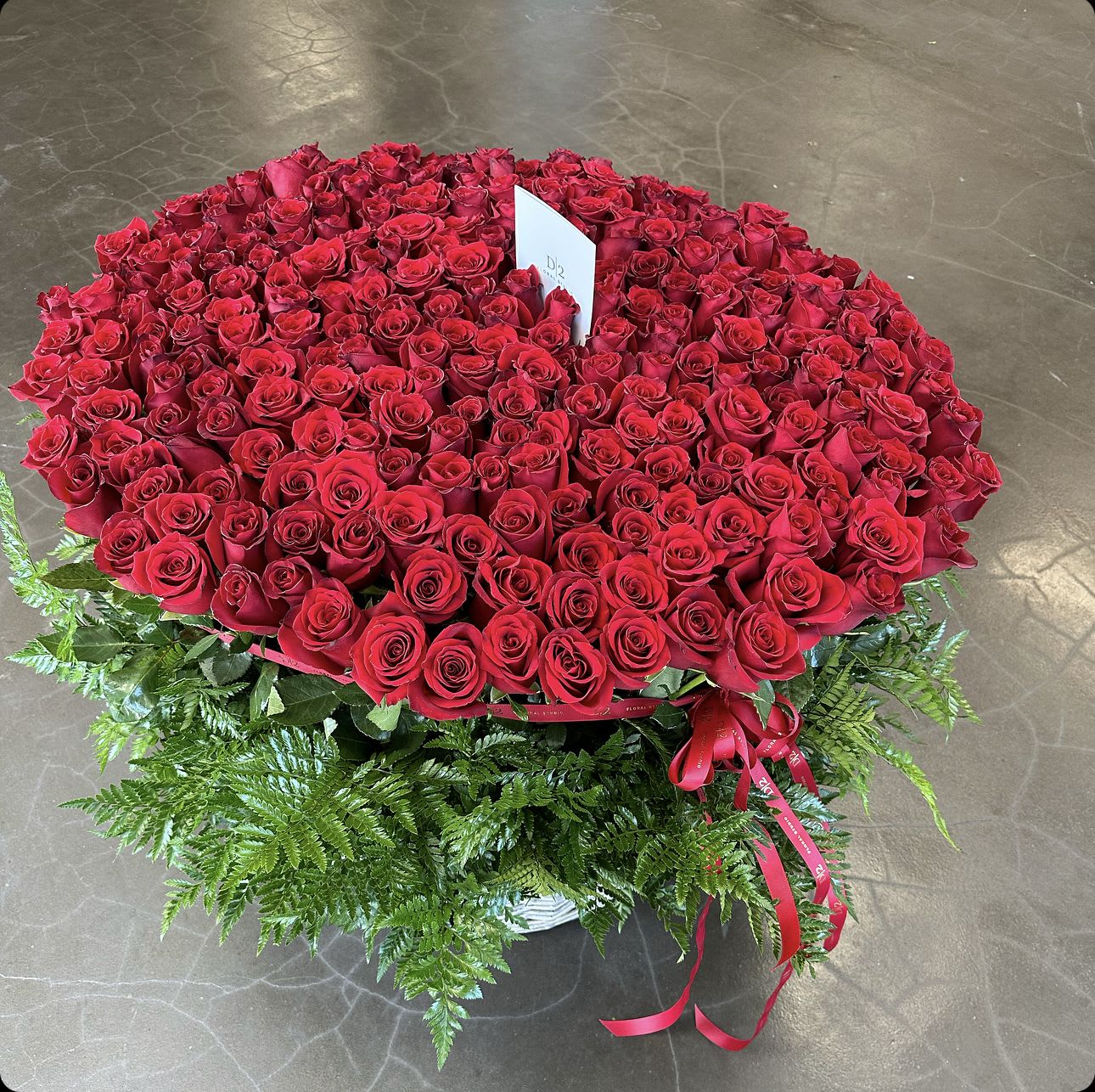Large round arrangement of red roses with fern greenery and a red ribbon