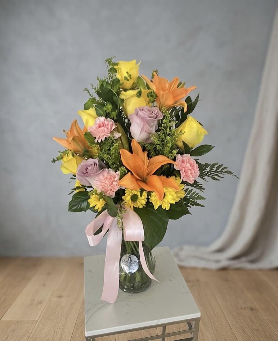 Morning Radiance  - Send a hug in a vase! This high-energy arrangement is packed with joy, combining bright yellow and orange tones with sweet pastel accents. With its lush greenery and mix of premium roses and lilies, it’s the perfect centerpiece to bring a smile to any room. • Best for:  Mother’s Day, Congratulations, Get Well Soon, or Cheer Up. 