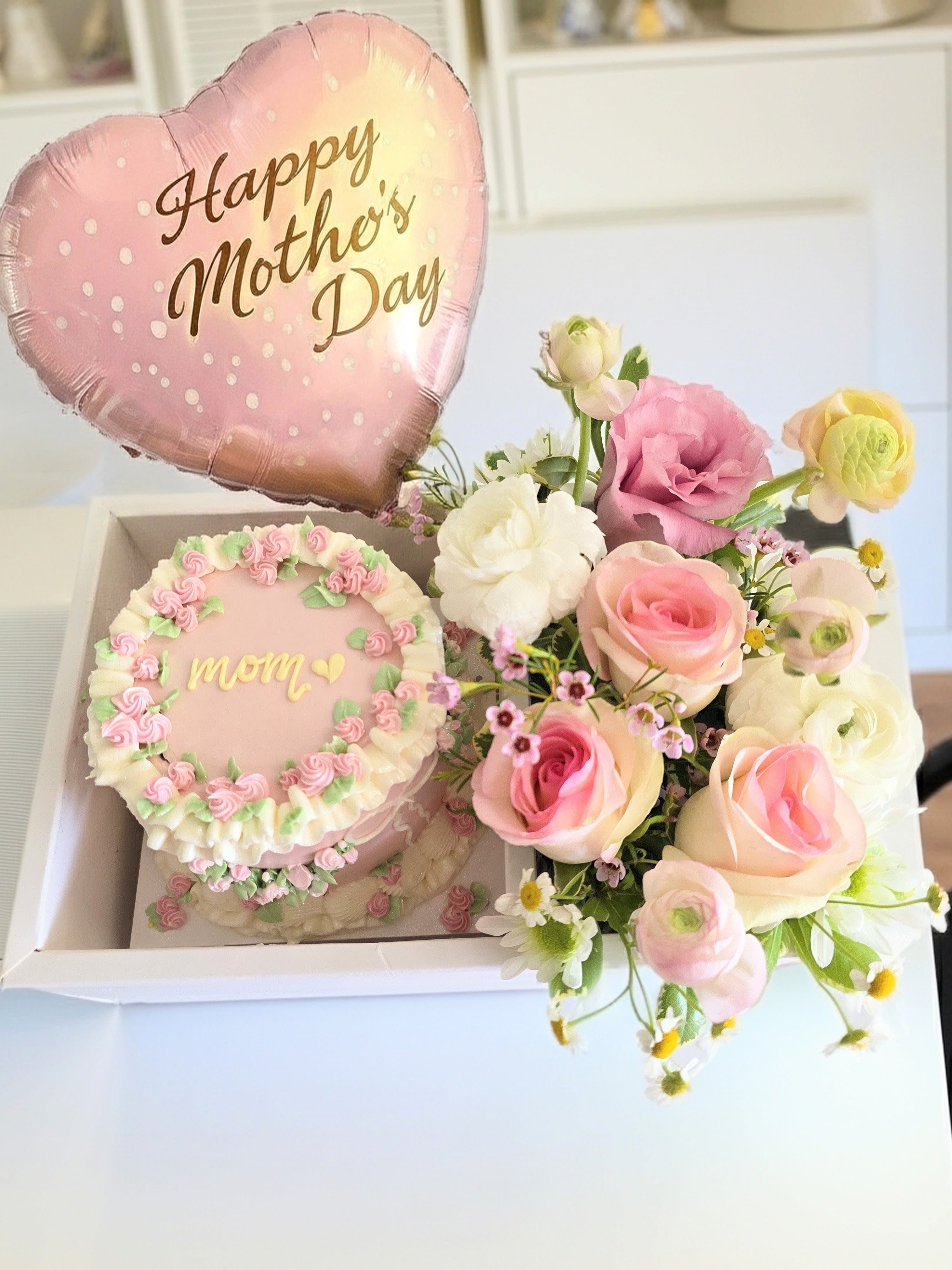 Mother's Day gift box with pink balloon, cake, and pastel flower bouquet