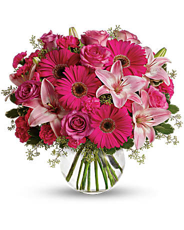 Pink gerbera daisies, roses, and lilies in a clear glass vase