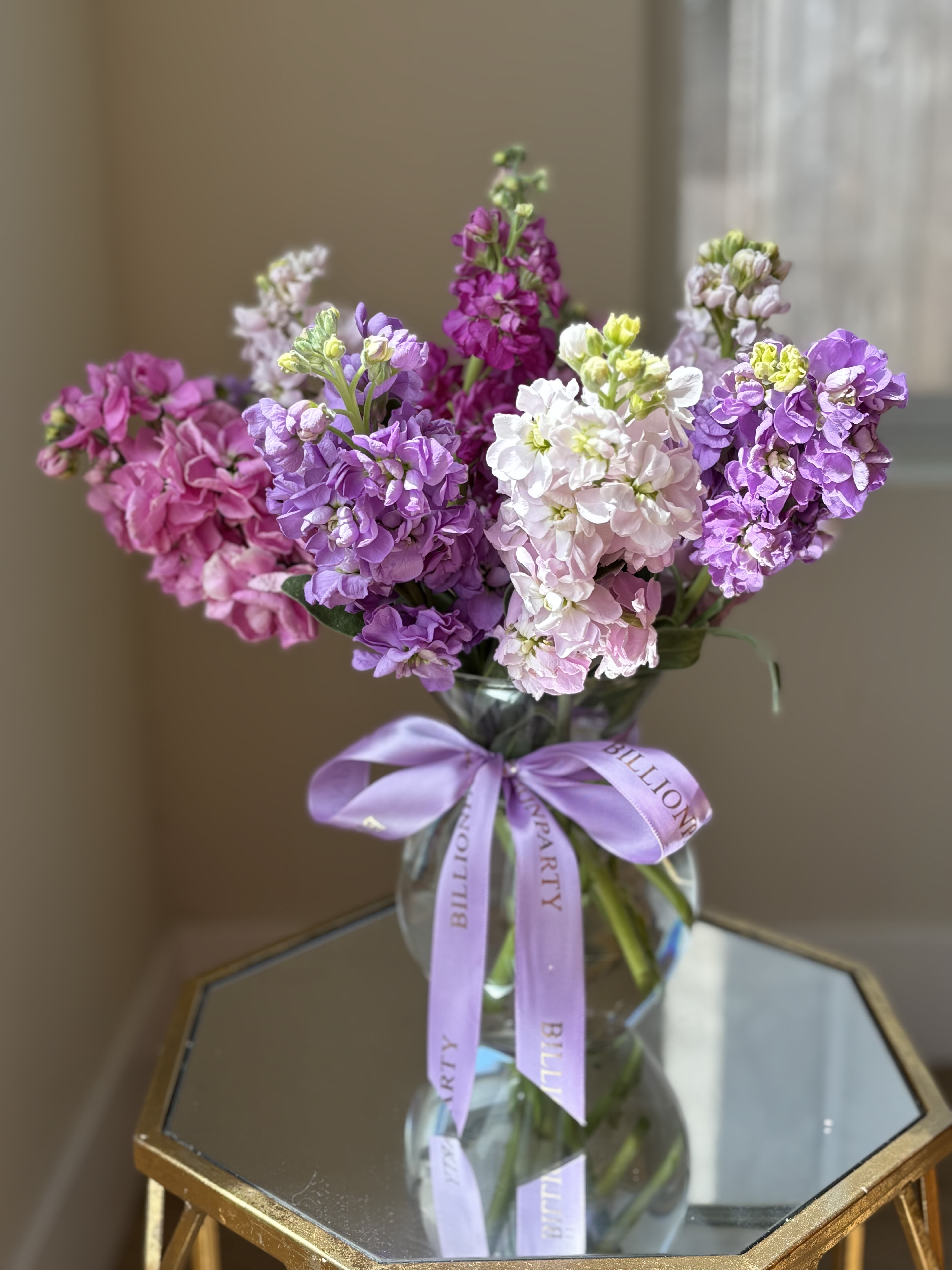 Bouquet of purple, pink, and white flowers in a glass vase with a lavender ribbon