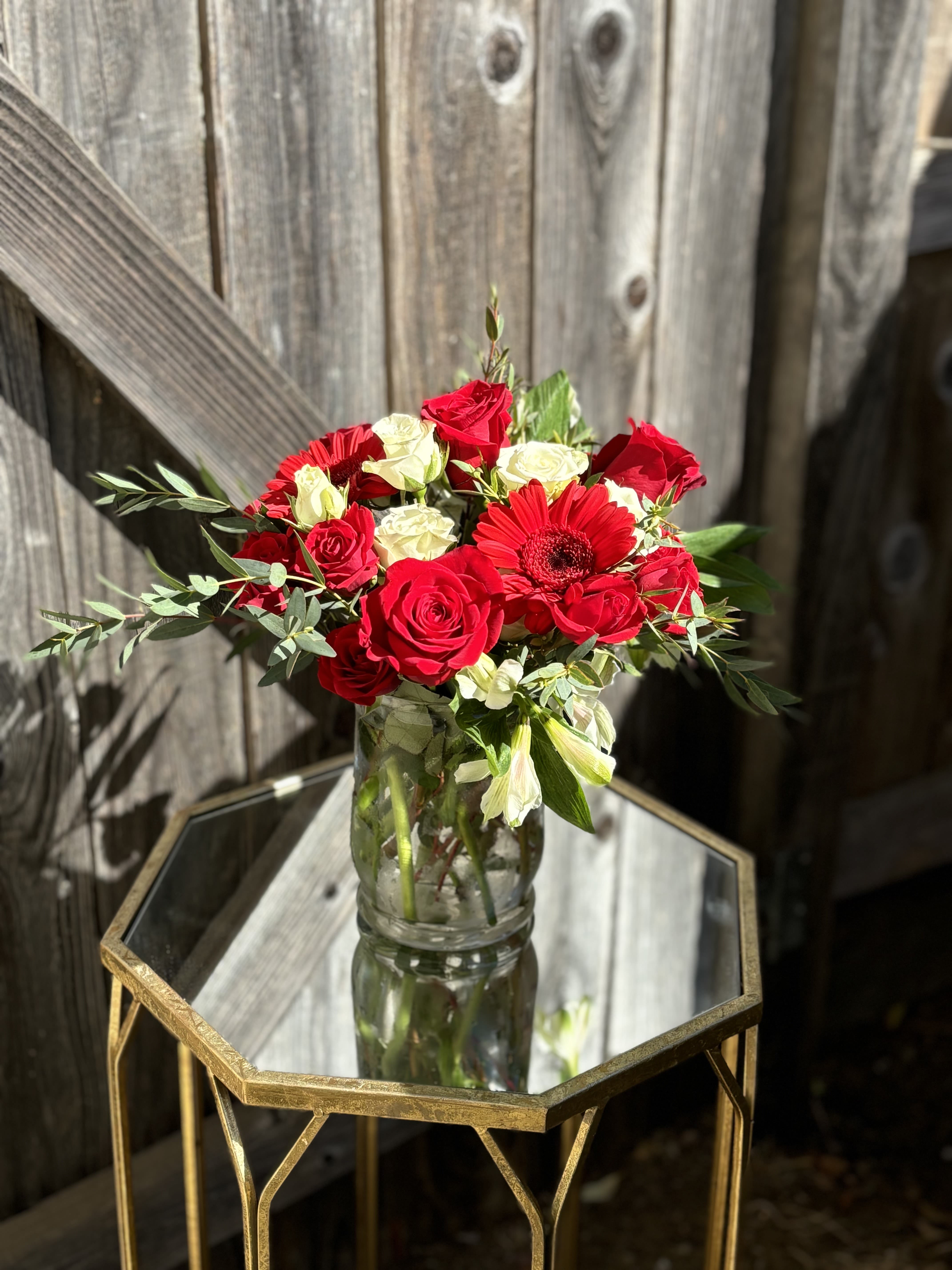 Red and white roses with a red gerbera daisy in a glass vase