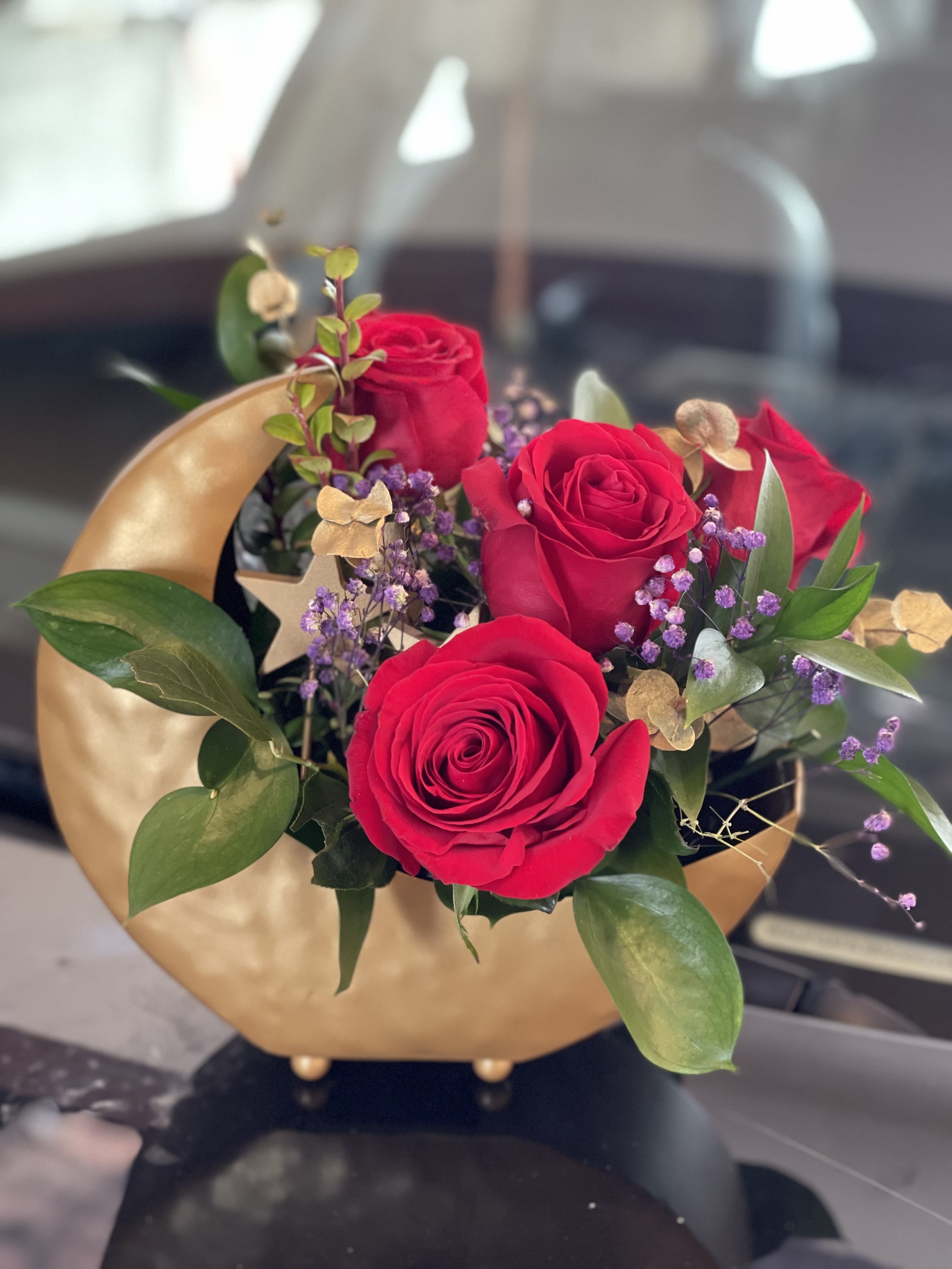 Red roses arranged in a gold vase with purple filler flowers