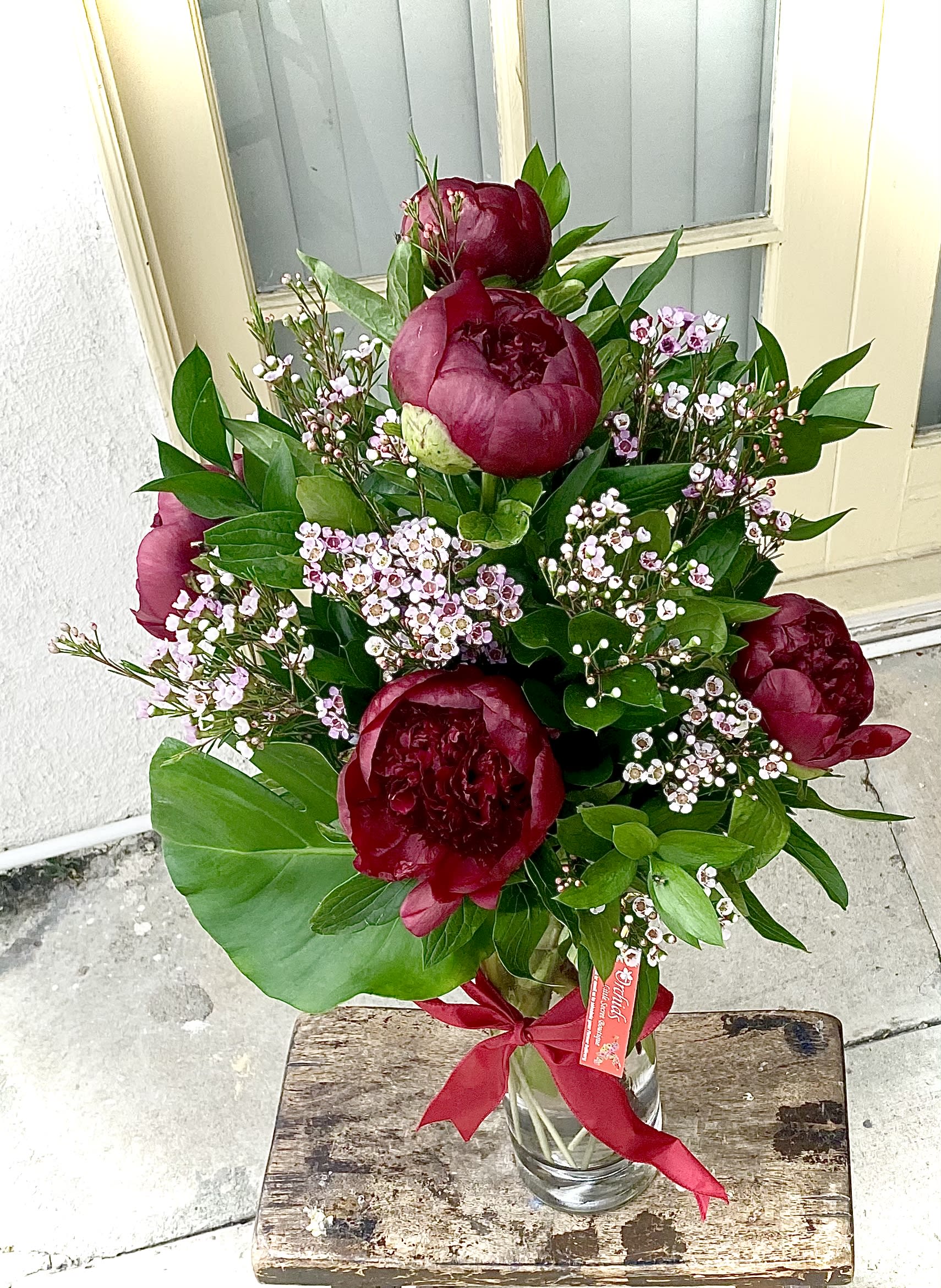 Bouquet of deep red peonies with pink filler flowers in a glass vase