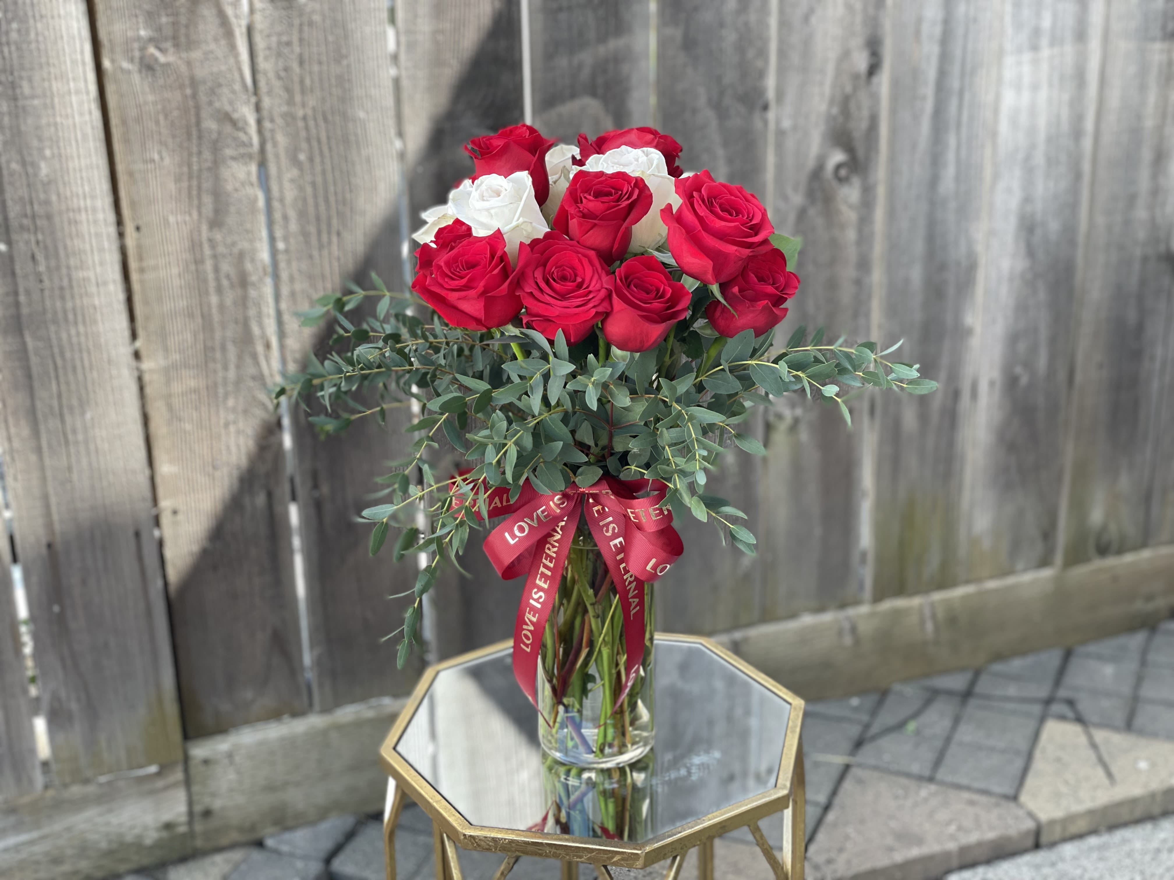 Red and white roses in a clear glass vase with a red ribbon