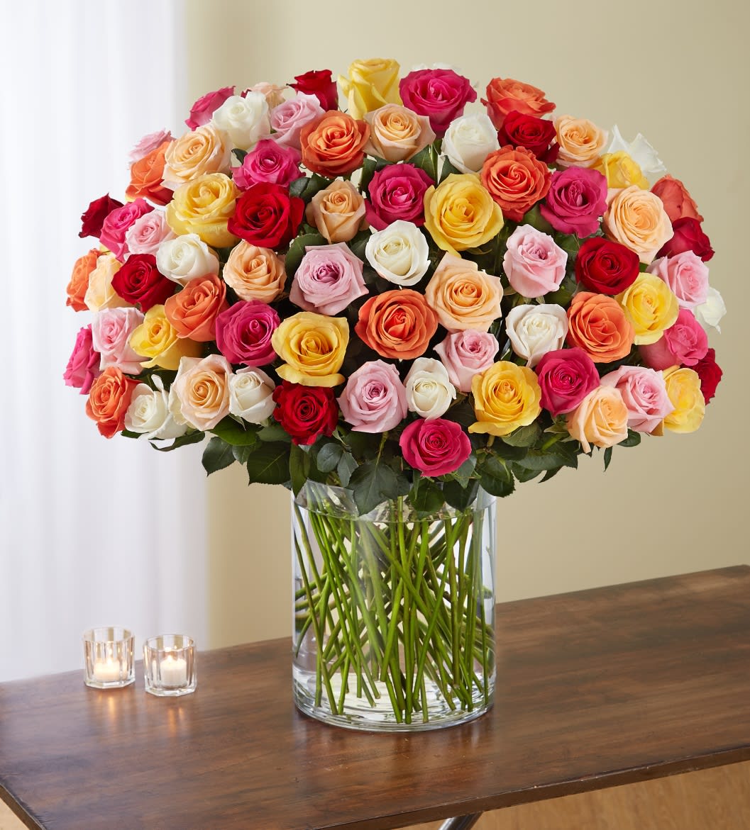 Large mixed-color rose arrangement in a clear glass vase on a wooden table