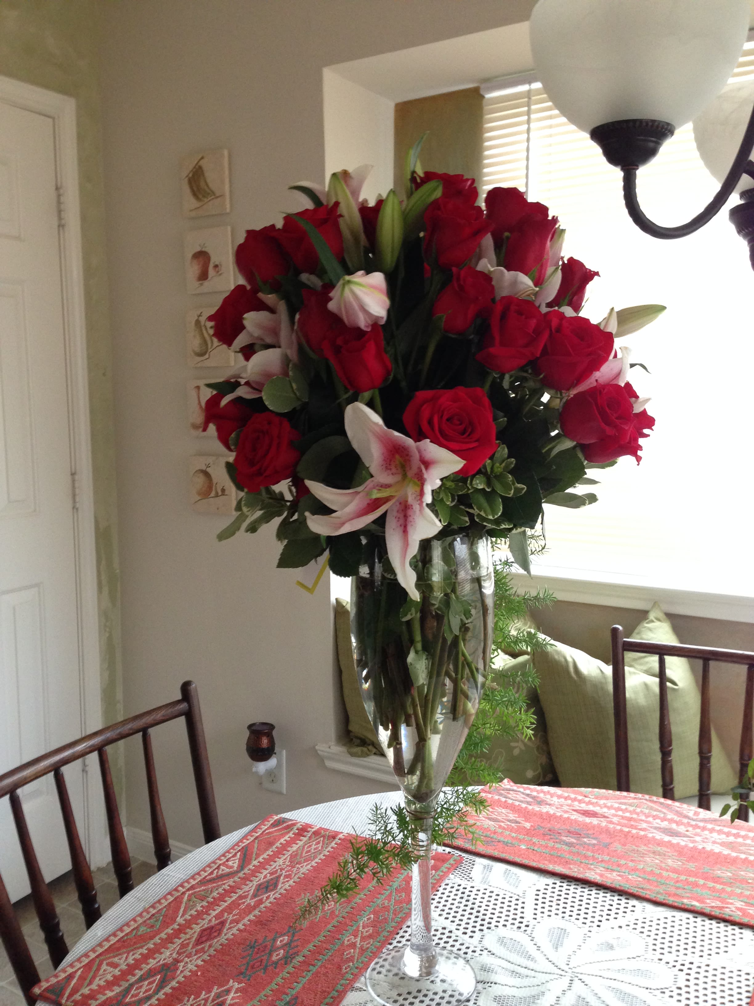 Tall bouquet of red roses and pink lilies in a clear glass vase