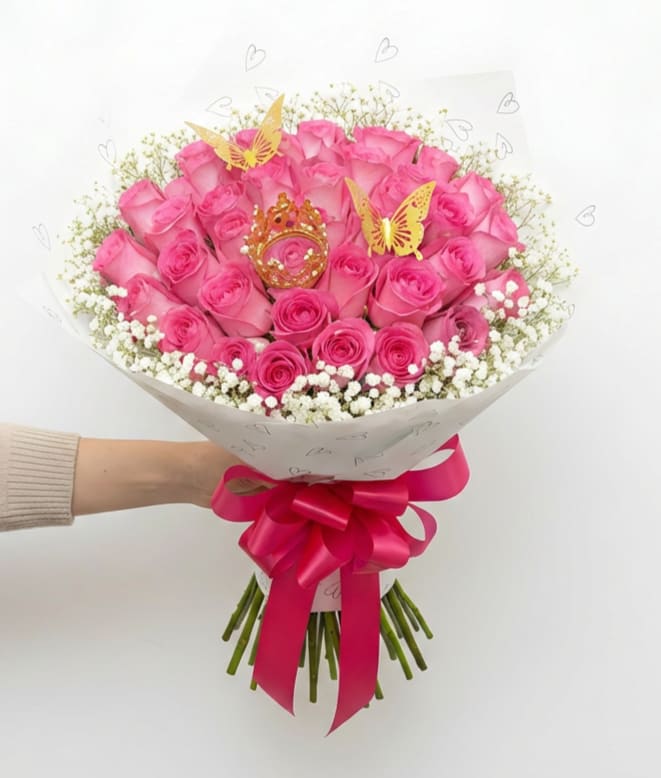 Princess Blush - Soft, playful, and full of charm, Princess Blush is designed to make any moment feel extra special. Featuring a lush arrangement of 50 vibrant pink roses, this bouquet is accented with delicate baby’s breath and wrapped in a stylish, heart-patterned design.  Finished with a statement satin bow, a decorative crown, and elegant butterfly accents, this bouquet brings a touch of whimsy and luxury together. It’s the perfect choice for birthdays, celebrations, or anyone who deserves to feel like royalty.  Fun, feminine, and eye-catching, Princess Blush is a beautiful way to celebrate love, joy, and unforgettable moments.