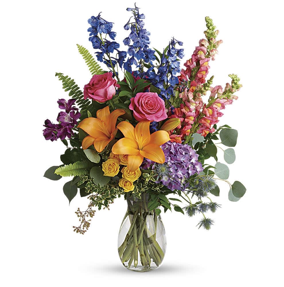 Tall mixed bouquet of orange lilies, pink roses, and assorted bright flowers in a clear glass vase