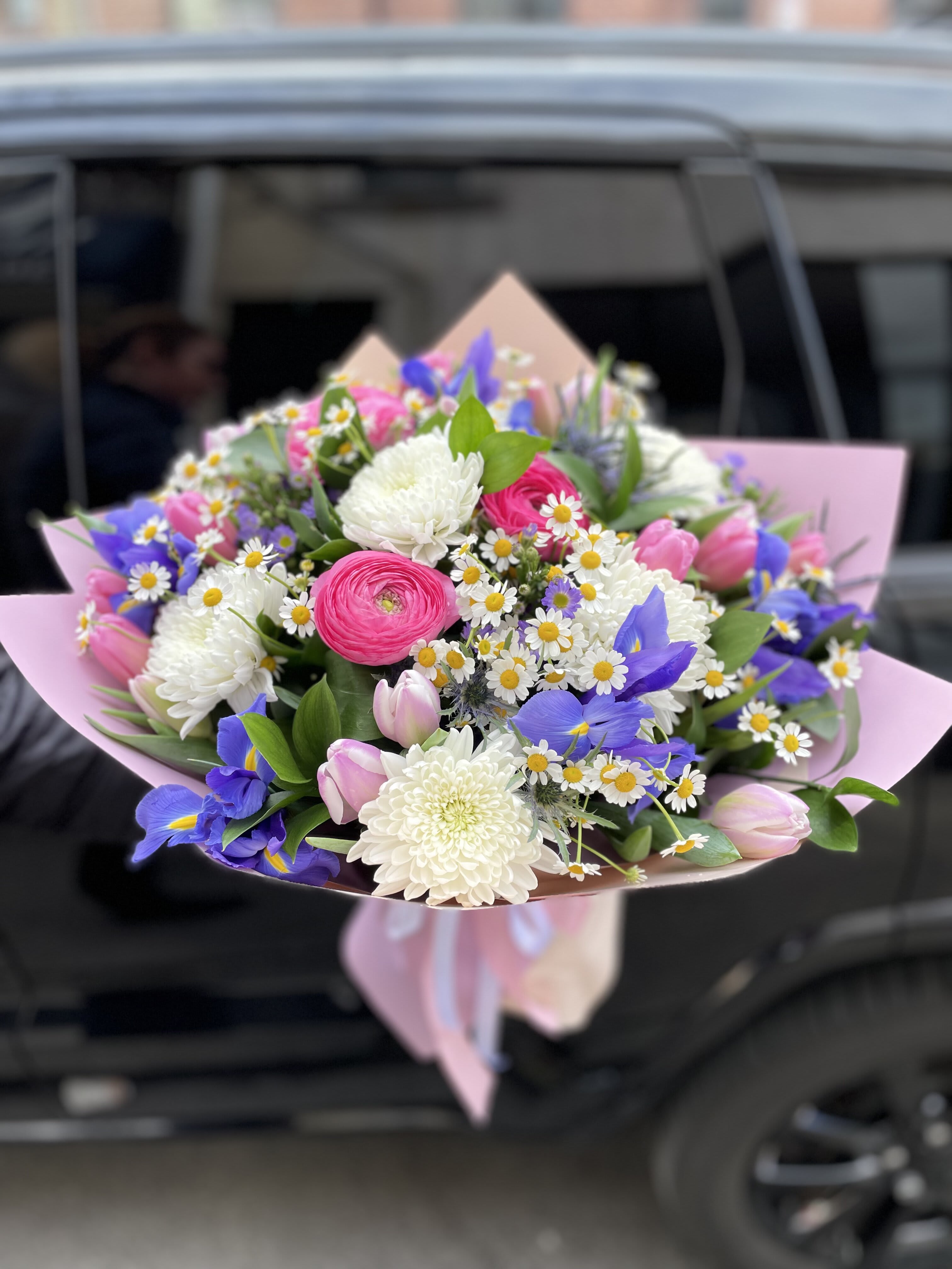 Bouquet of pink, white, and blue flowers wrapped in pink paper
