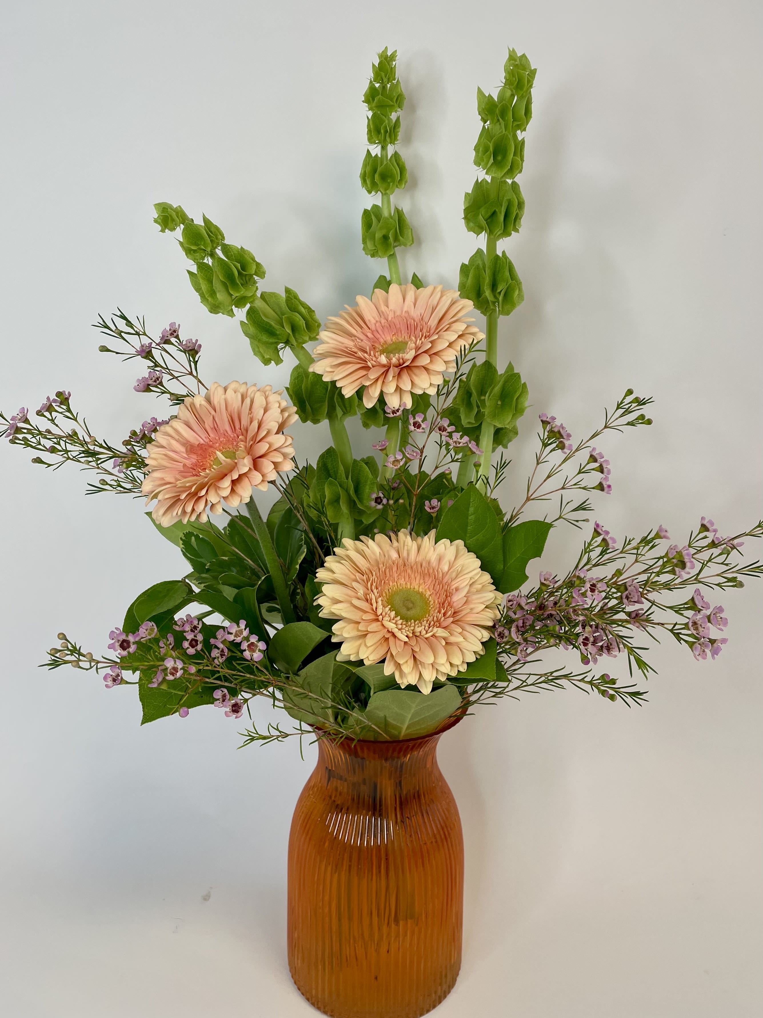 Peach gerbera daisies in an amber vase with green spikes and small purple flowers