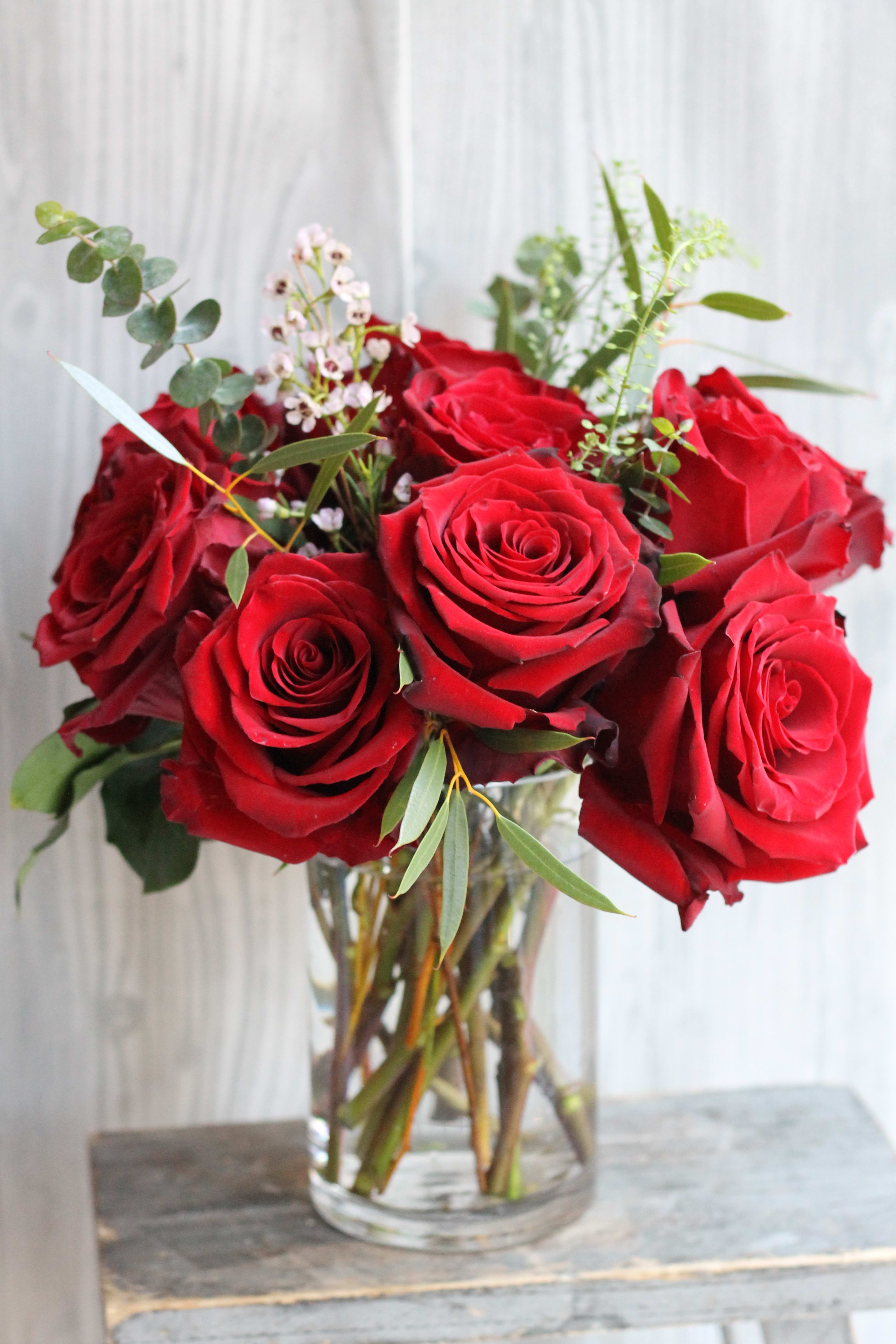 Arrangement of red roses with small white filler flowers in a clear glass vase
