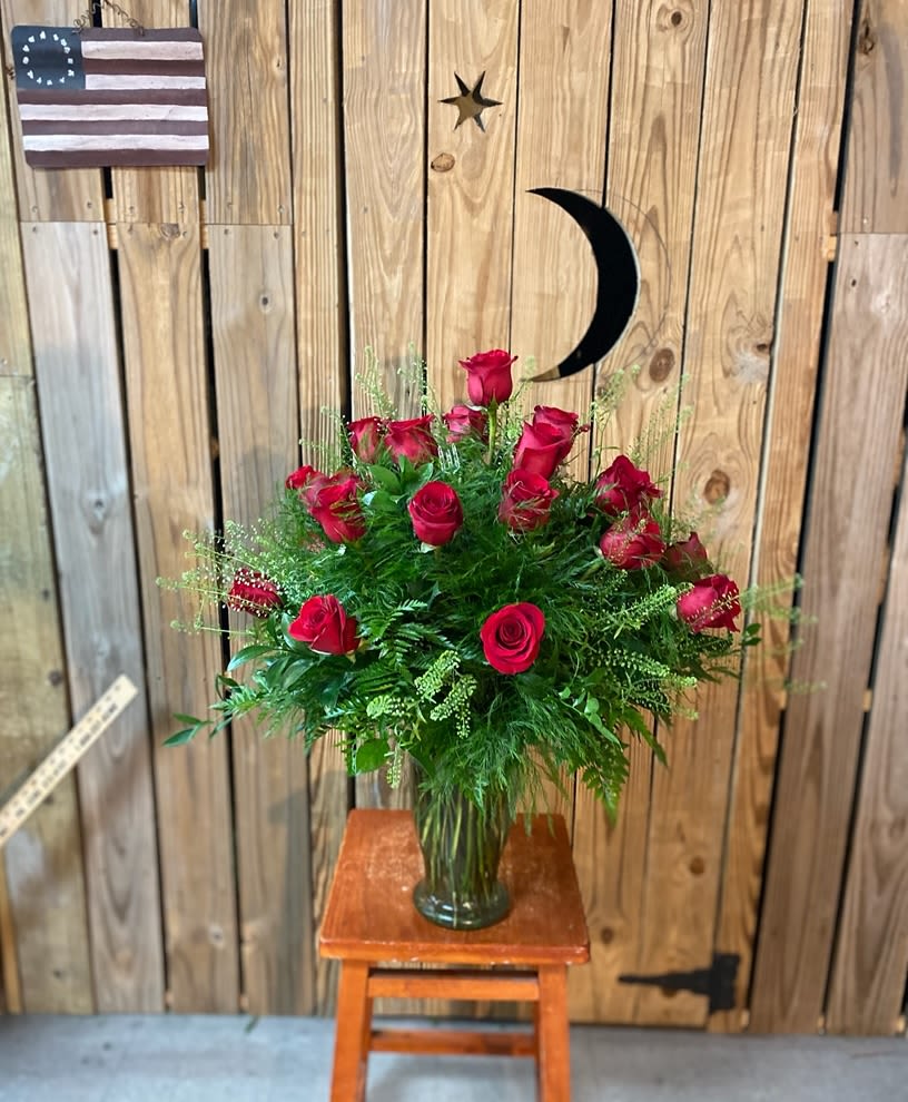 Red roses arranged in a glass vase with greenery