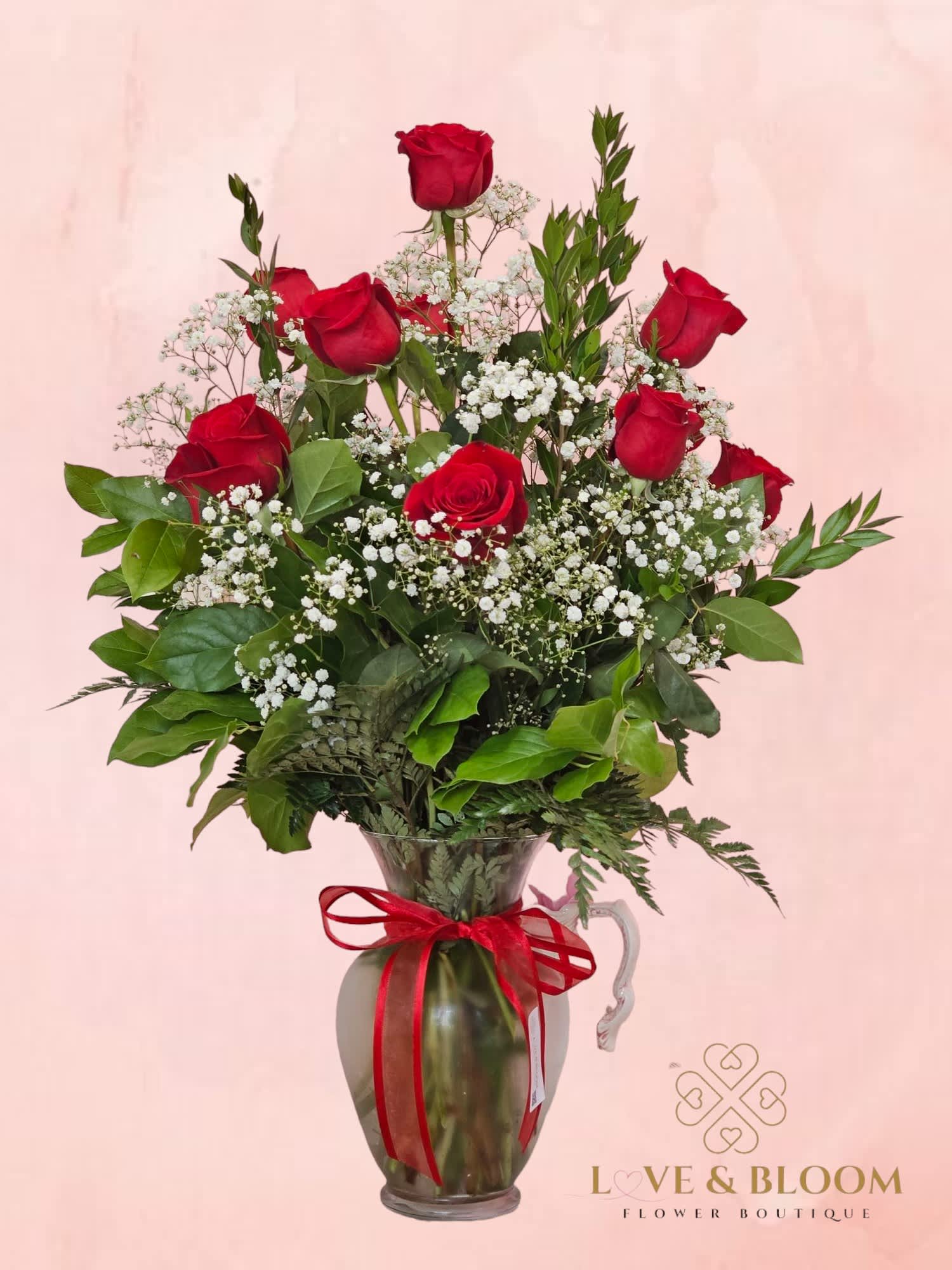 Red roses arranged in a glass pitcher with baby's breath and greenery