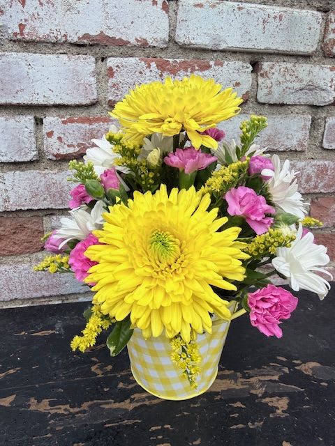SUN SHINING  DAY - Two bold yellow chrysanthemums take center stage in this cheerful flower arrangement, making it an ideal choice for a spring birthday, Mother's Day, or a bright "thinking of you" surprise. As a get-well, housewarming, or just-because gift, the sunny yellow paired with soft pinks and crisp white brings an instant mood lift-the kind that makes the person you're thinking of feel genuinely seen and comforted.  Surrounding the focal chrysanthemums are fluffy pink carnations and small white daisy-like chrysanthemums, arranged with a casual garden feel that reads fresh and friendly. The blooms sit in a yellow-and-white checkered ceramic container that adds a playful, homey touch and fits easily on a kitchen counter or bedside table. Compact yet joyful, this arrangement is a thoughtful way to say thank you, I'm sorry, congratulations on retirement, or happy Women's Day, Best Friends Day, or Boss's Day-no special care required beyond fresh water to keep the flowers looking their best.