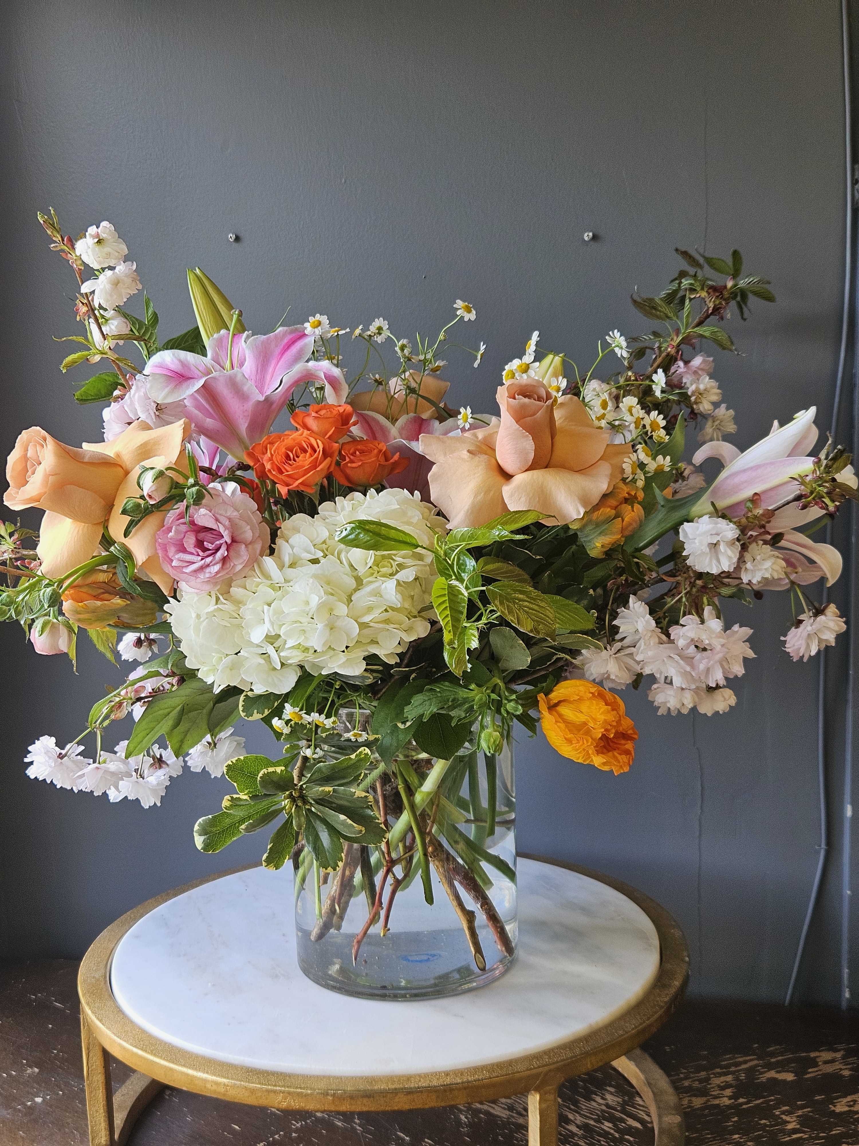 Mixed arrangement of peach roses, pink lilies, and white hydrangeas in a clear glass vase