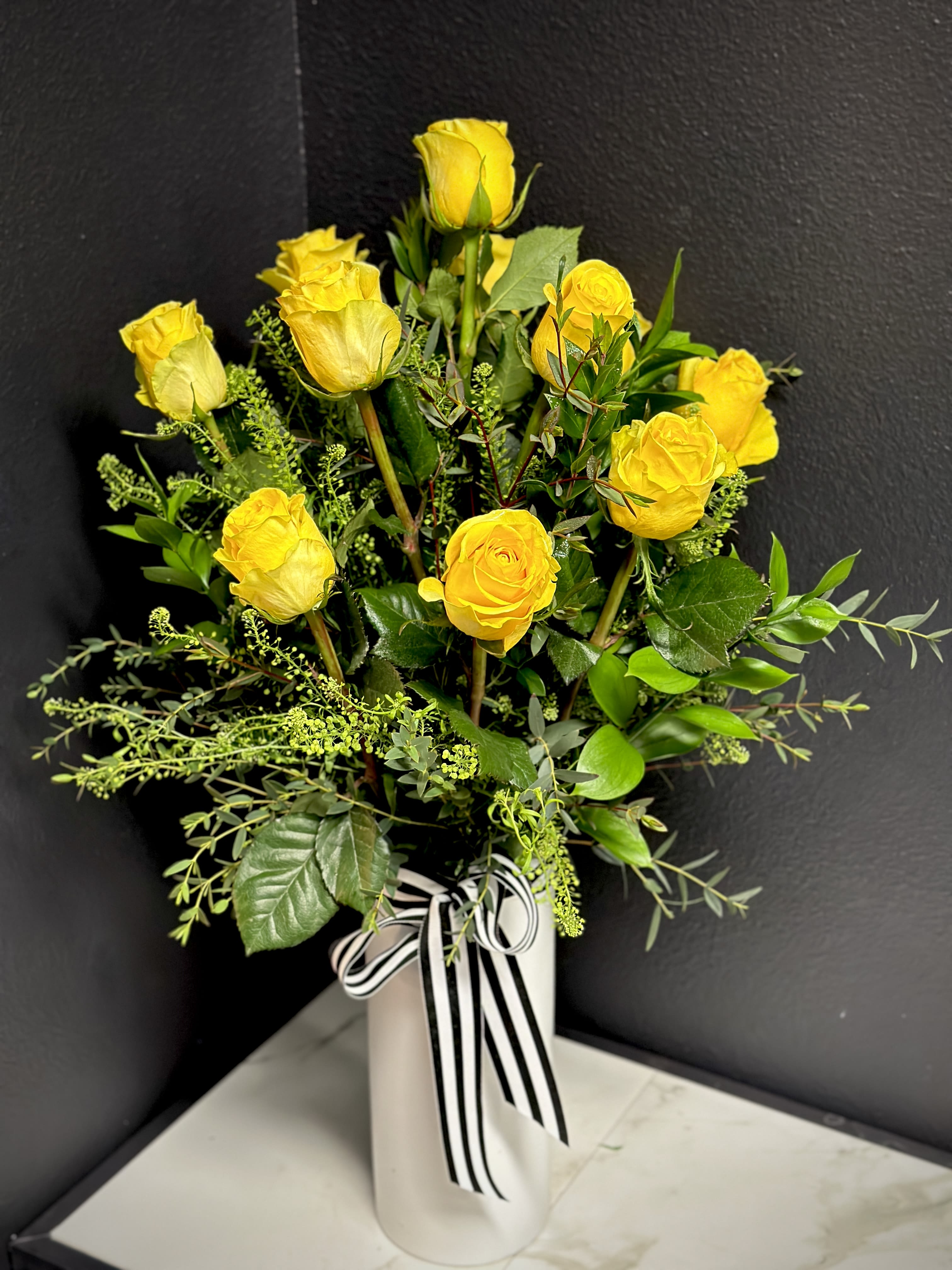 Yellow roses arranged in a white vase with a black-and-white ribbon